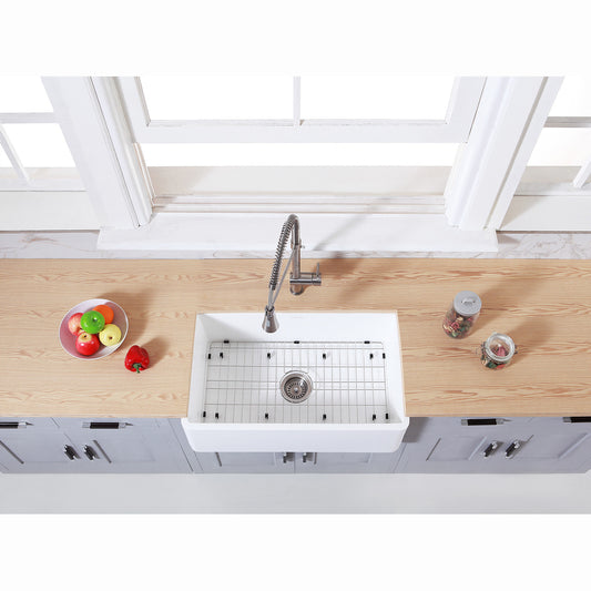 Kingston Brass KGKFA301810BC matte white kitchen sink with bottom grid and strainer on a wooden countertop with fruits and vegetables.
