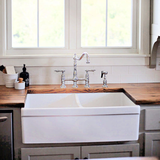 KINGSTON Brass Heritage Bridge Kitchen Faucet with Brass Sprayer installed above a farmhouse sink