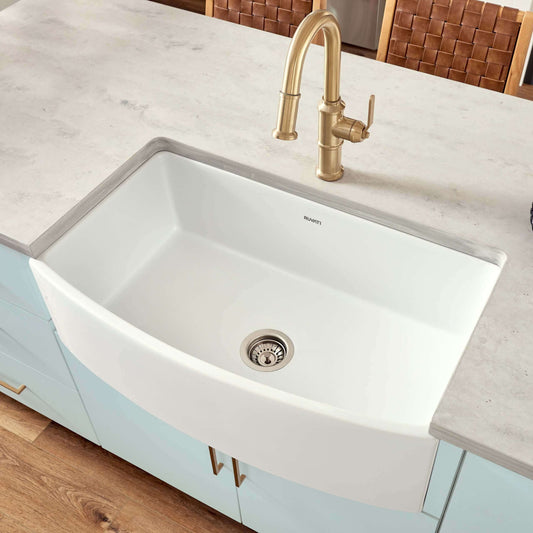 Ruvati 33" Fireclay Bow Front Farmhouse Kitchen Sink - RVL2398 installed in modern kitchen with gold faucet.