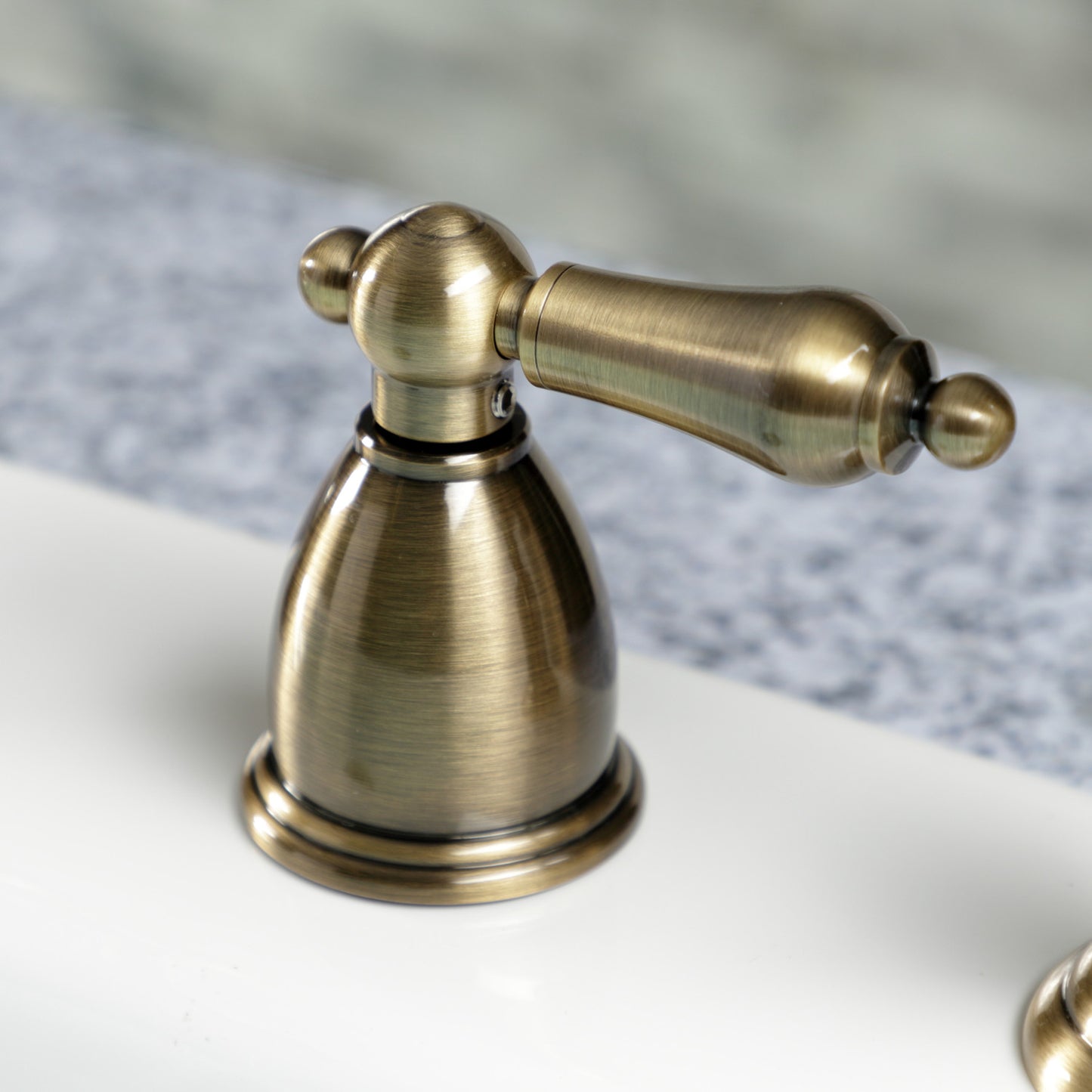 Kingston Brass "Antique Brass" widespread kitchen faucet handle on a blurred background
