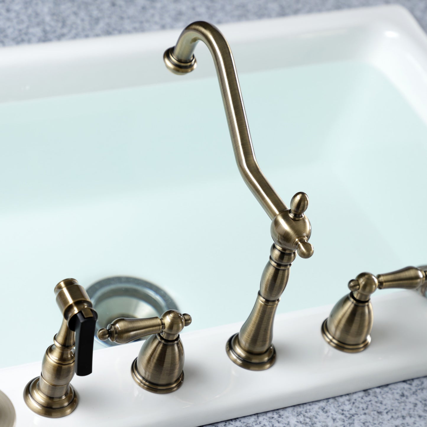 Kingston Brass "Antique Brass" widespread kitchen faucet set on a white sink with a gray background