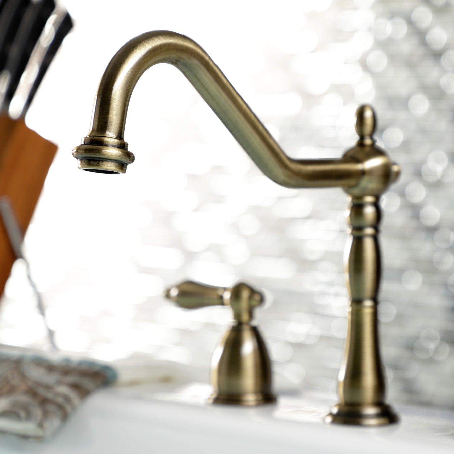 Kingston Brass "Antique Brass" widespread kitchen faucet and handles on a blurred background