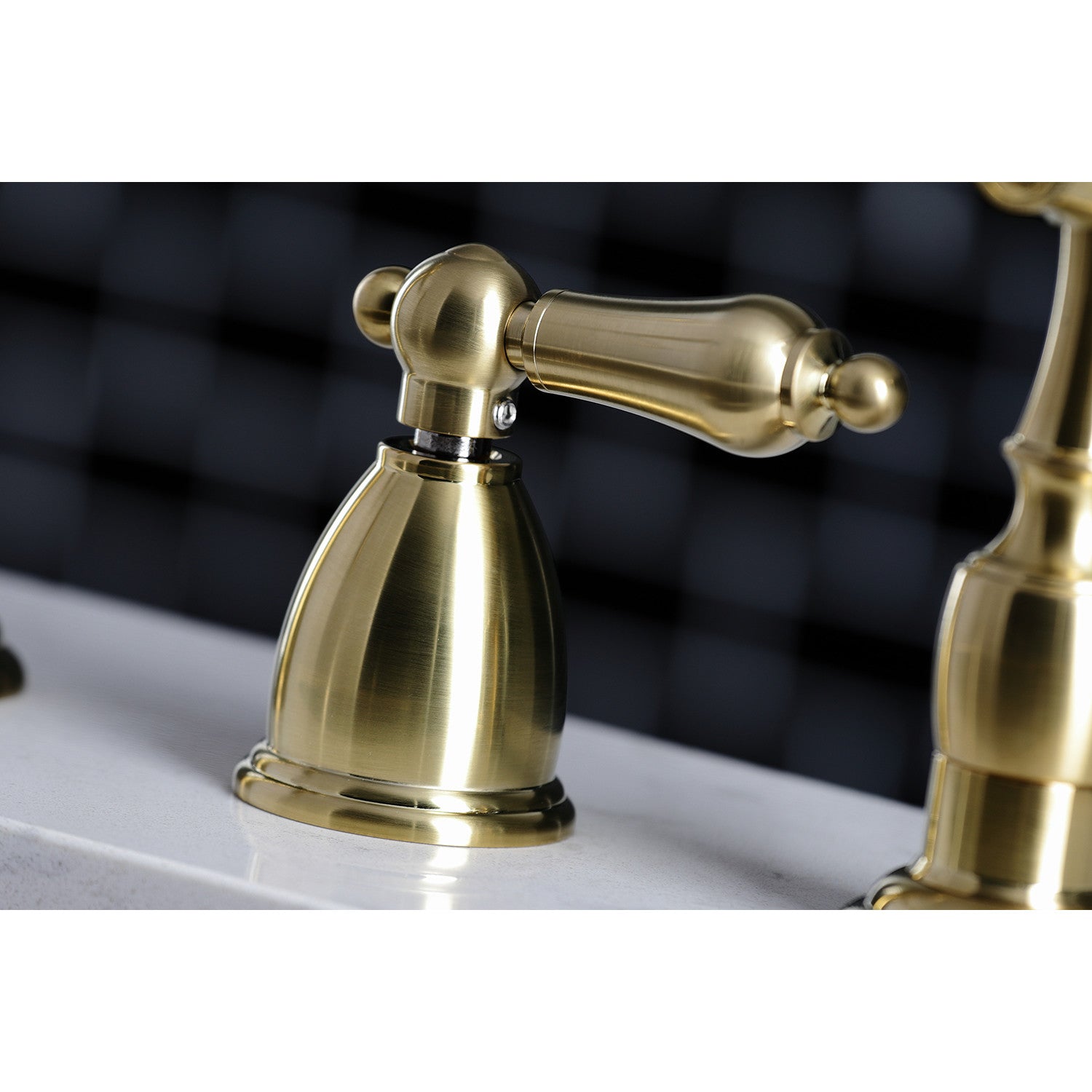 Kingston Brass "Burshed Brass" widespread kitchen faucet  handles on a white sink with a blurred black and white checkered background