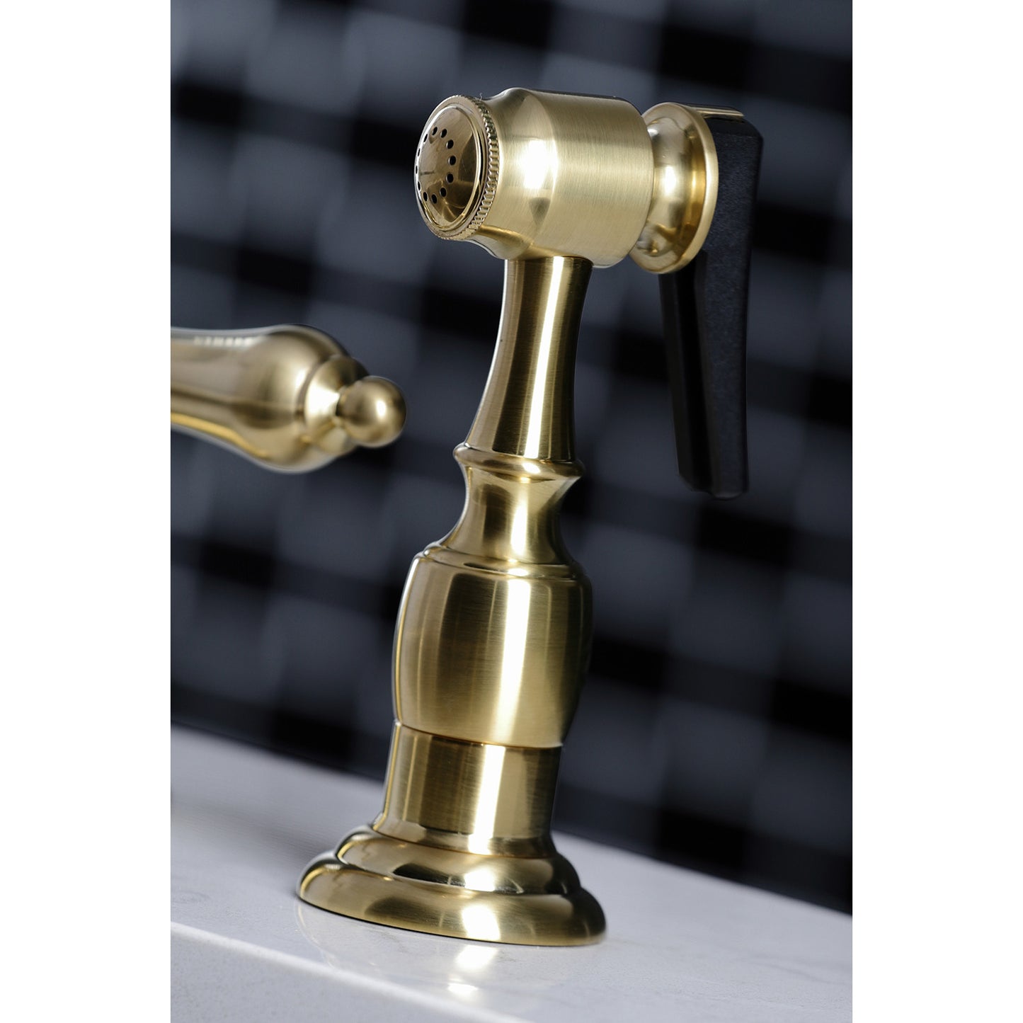 Kingston Brass "Brushed Brass" widespread kitchen faucet side sprayer with black handle on a blurred background