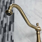 Faucet detail of Kingston Brass antique brass double-handle 2-hole wall-mount bridge kitchen faucet against a marble and tile background
