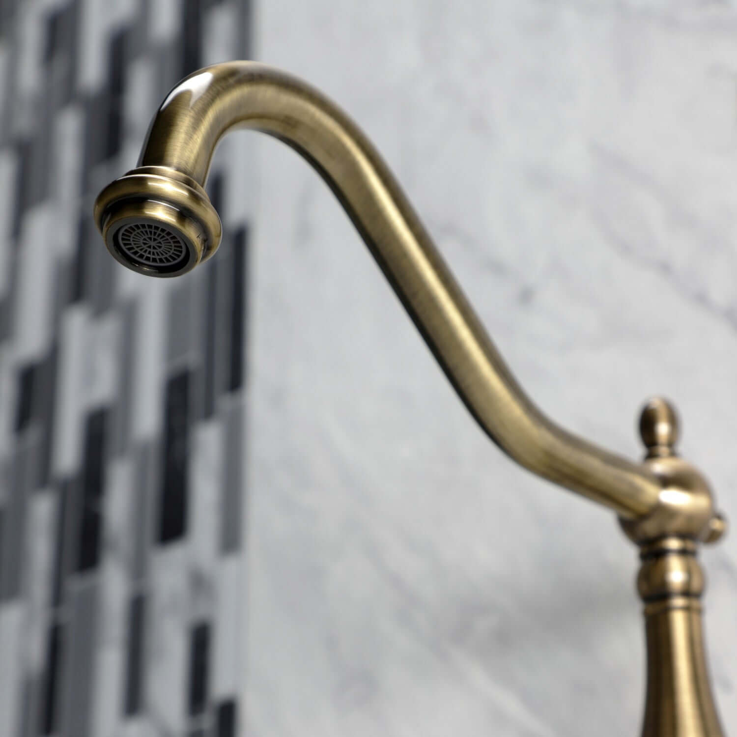 Faucet detail of Kingston Brass antique brass double-handle 2-hole wall-mount bridge kitchen faucet against a marble and tile background