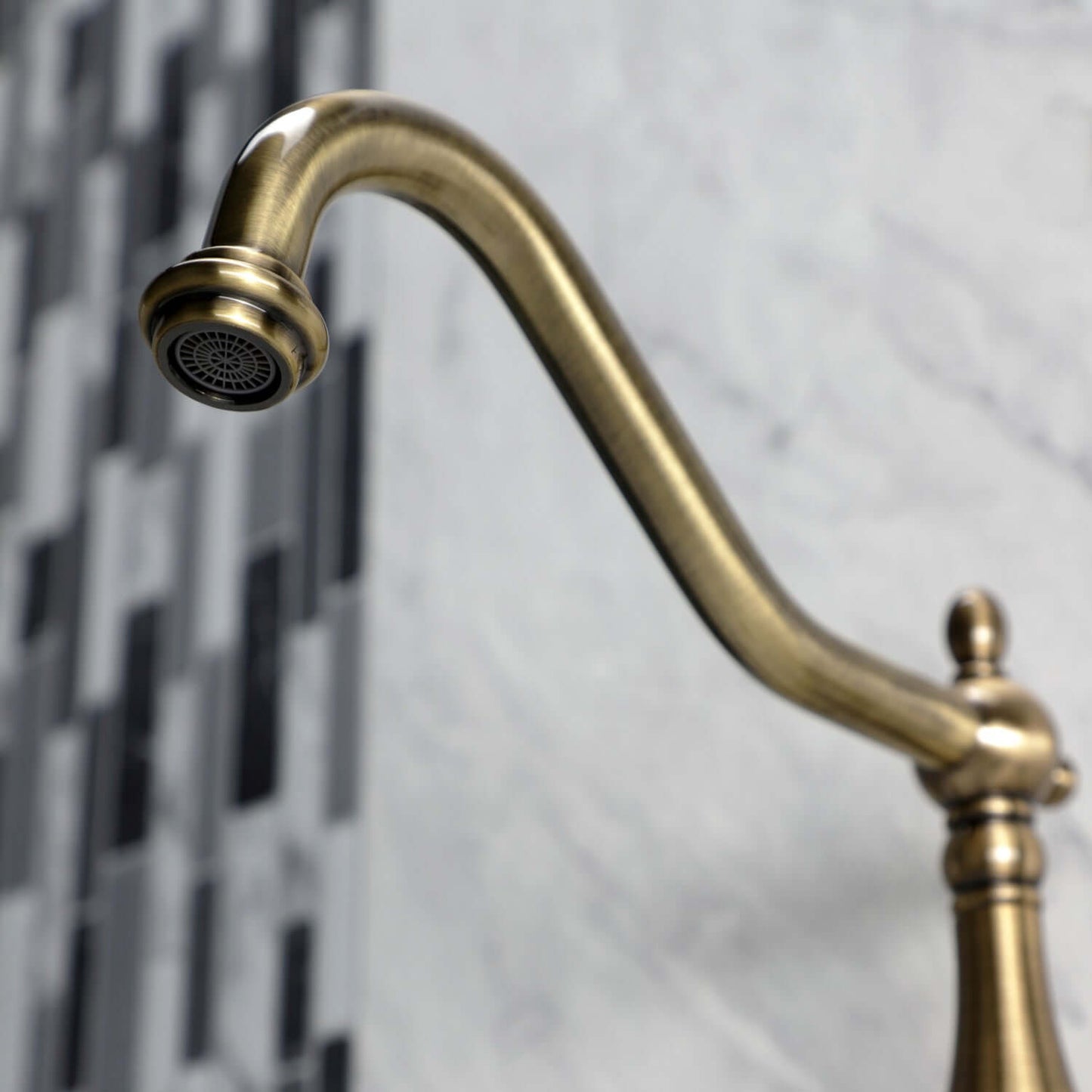Faucet detail of Kingston Brass antique brass double-handle 2-hole wall-mount bridge kitchen faucet against a marble and tile background