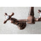 Close-up of Kingston Brass antique copper double-handle 2-hole wall-mount bridge kitchen faucet on a textured gray background