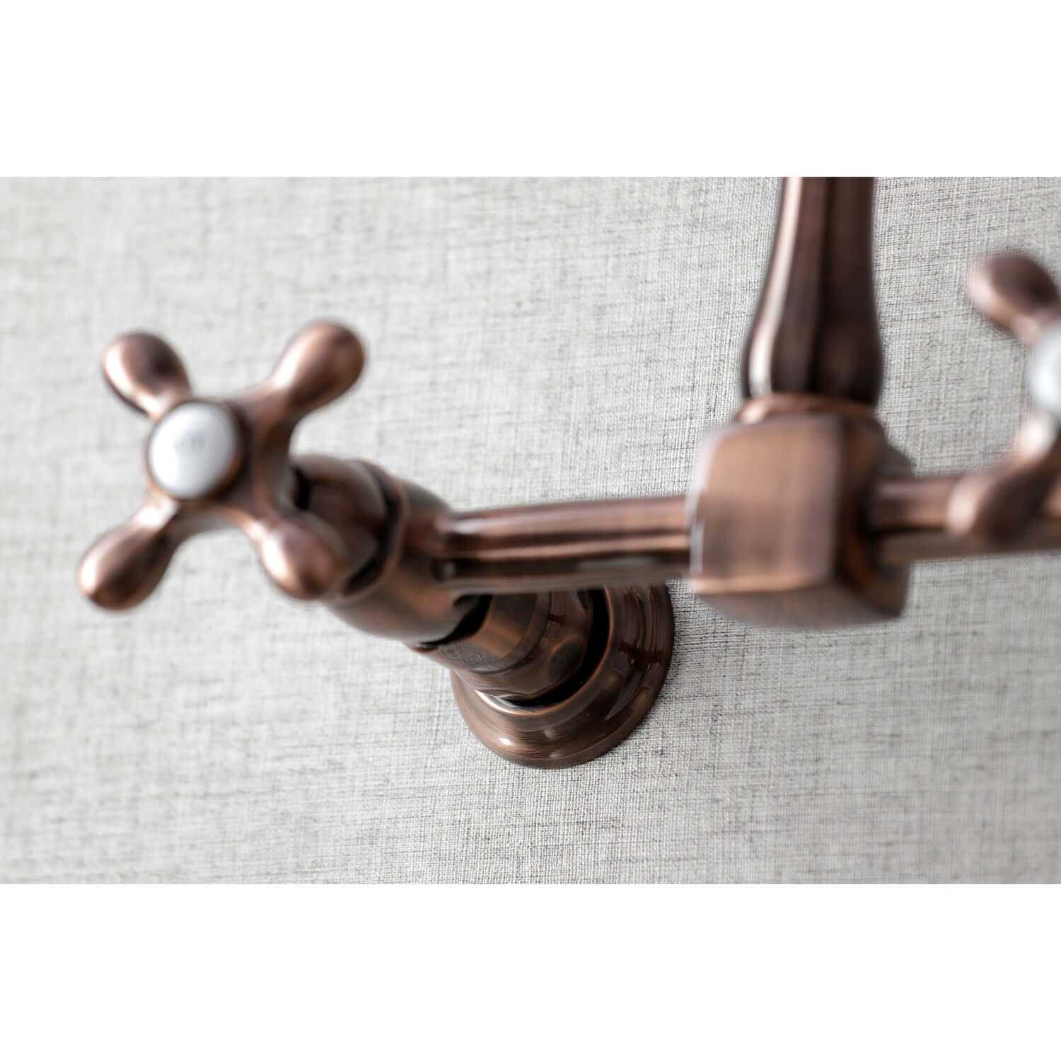 Close-up of Kingston Brass antique copper double-handle 2-hole wall-mount bridge kitchen faucet on a textured gray background