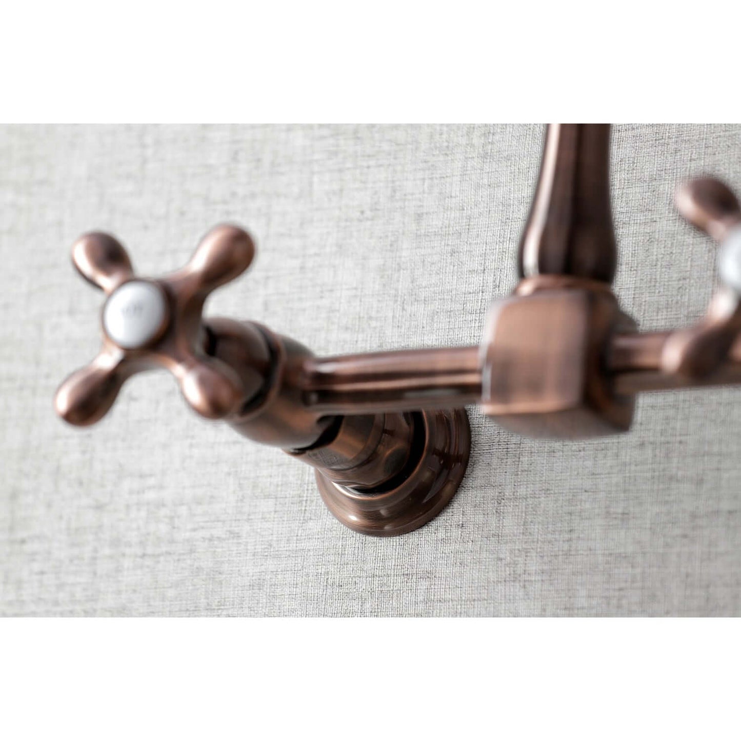 Close-up of Kingston Brass antique copper double-handle 2-hole wall-mount bridge kitchen faucet on a textured gray background