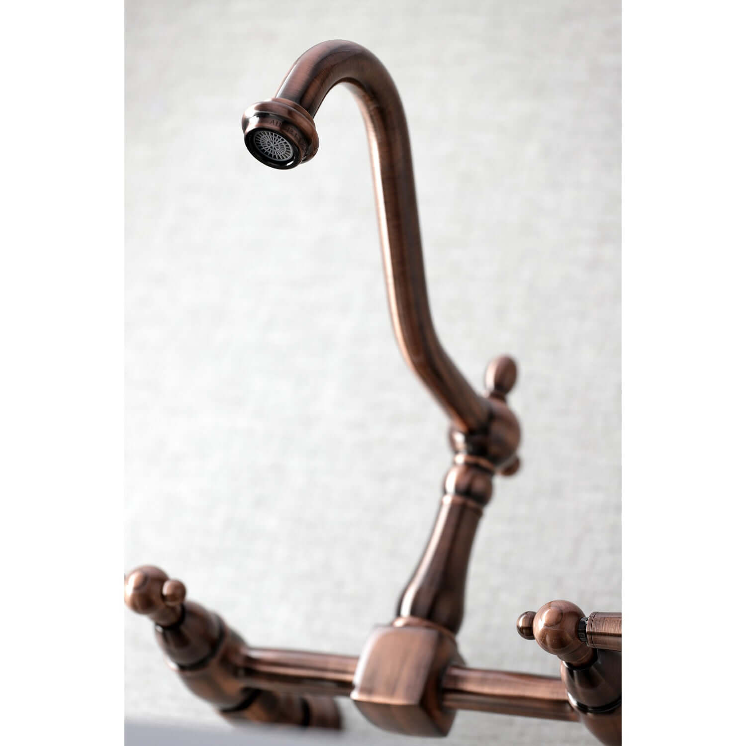 Kingston Brass antique copper double-handle 2-hole wall-mount bridge kitchen faucet with curved design on a light gray background