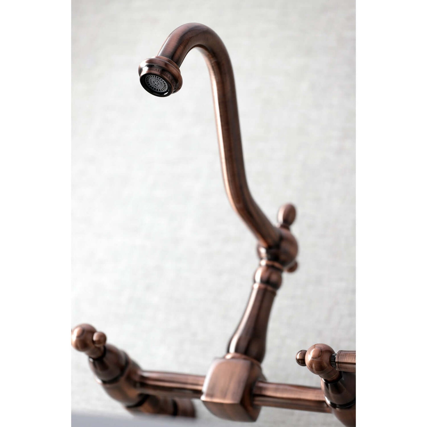 Kingston Brass antique copper double-handle 2-hole wall-mount bridge kitchen faucet with curved design on a light gray background