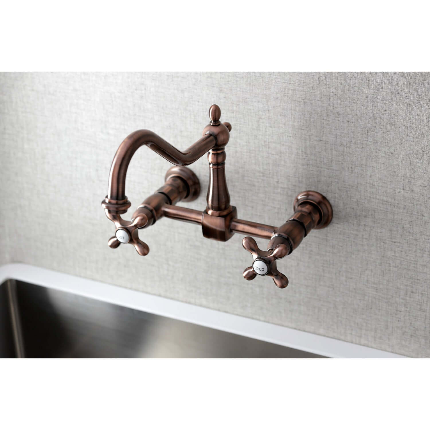 Kingston Brass antique copper double-handle 2-hole wall-mount bridge kitchen faucet on a light gray tiled wall with a stainless steel sink.