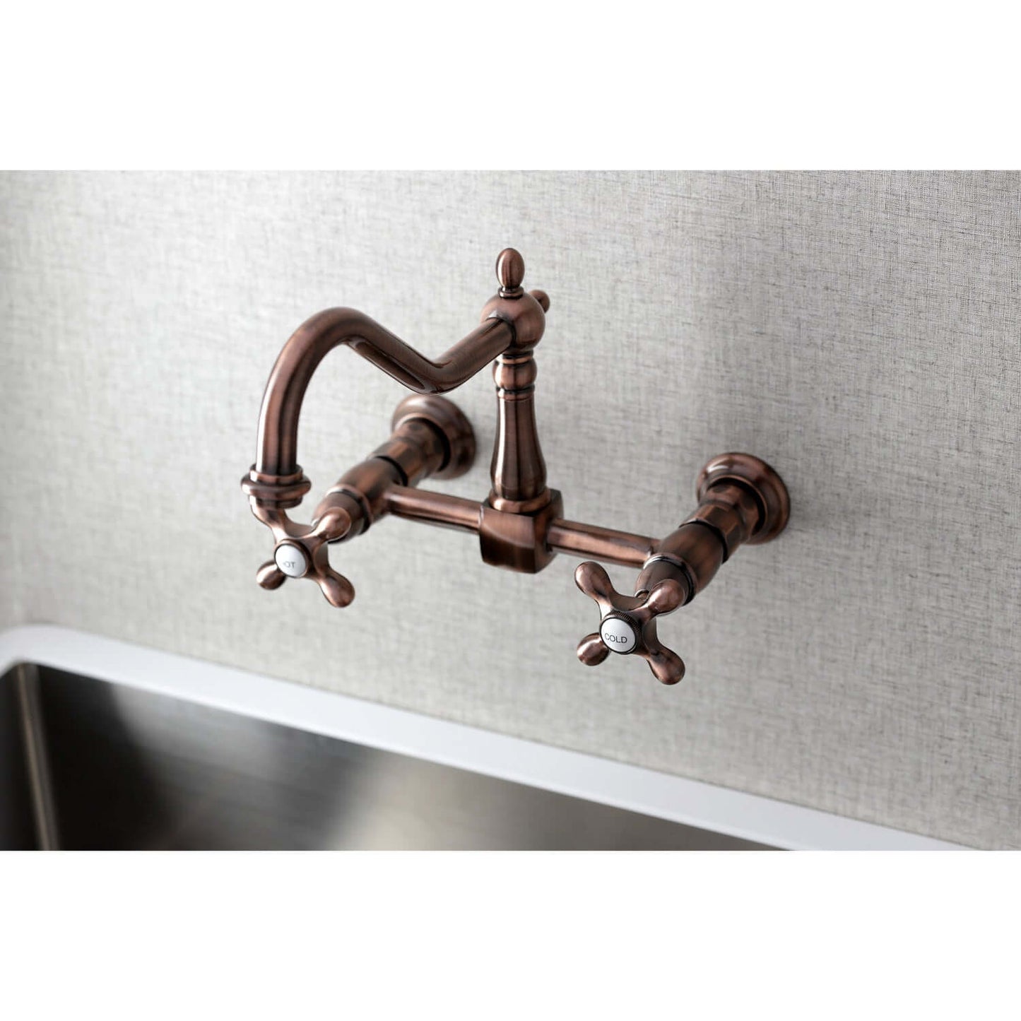 Kingston Brass antique copper double-handle 2-hole wall-mount bridge kitchen faucet on a light gray tiled wall with a stainless steel sink.
