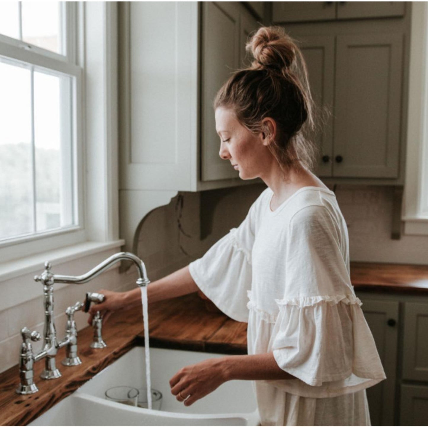 Woman using KINGSTON Brass Heritage Bridge Kitchen Faucet with Brass Sprayer in a traditional kitchen setting.