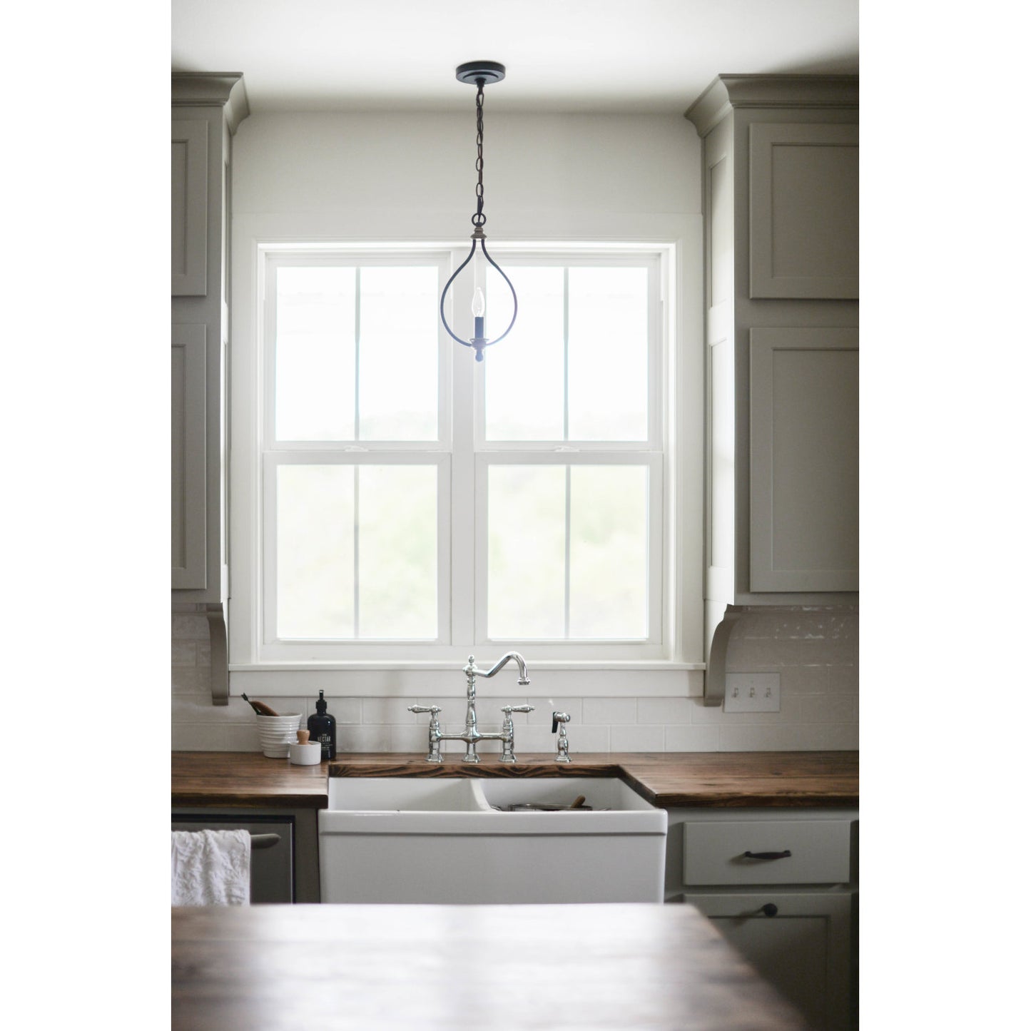 View of KINGSTON Brass Heritage Bridge Kitchen Faucet with Brass Sprayer above farmhouse sink in traditional kitchen setting.