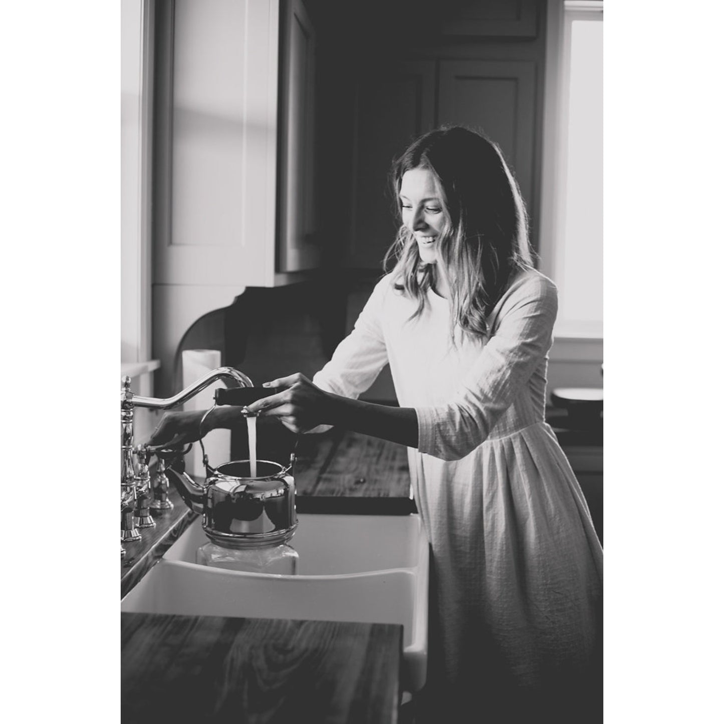 Black and white image of woman using Kingston Brass KS1271ALBS polished chrome faucet in a rustic kitchn