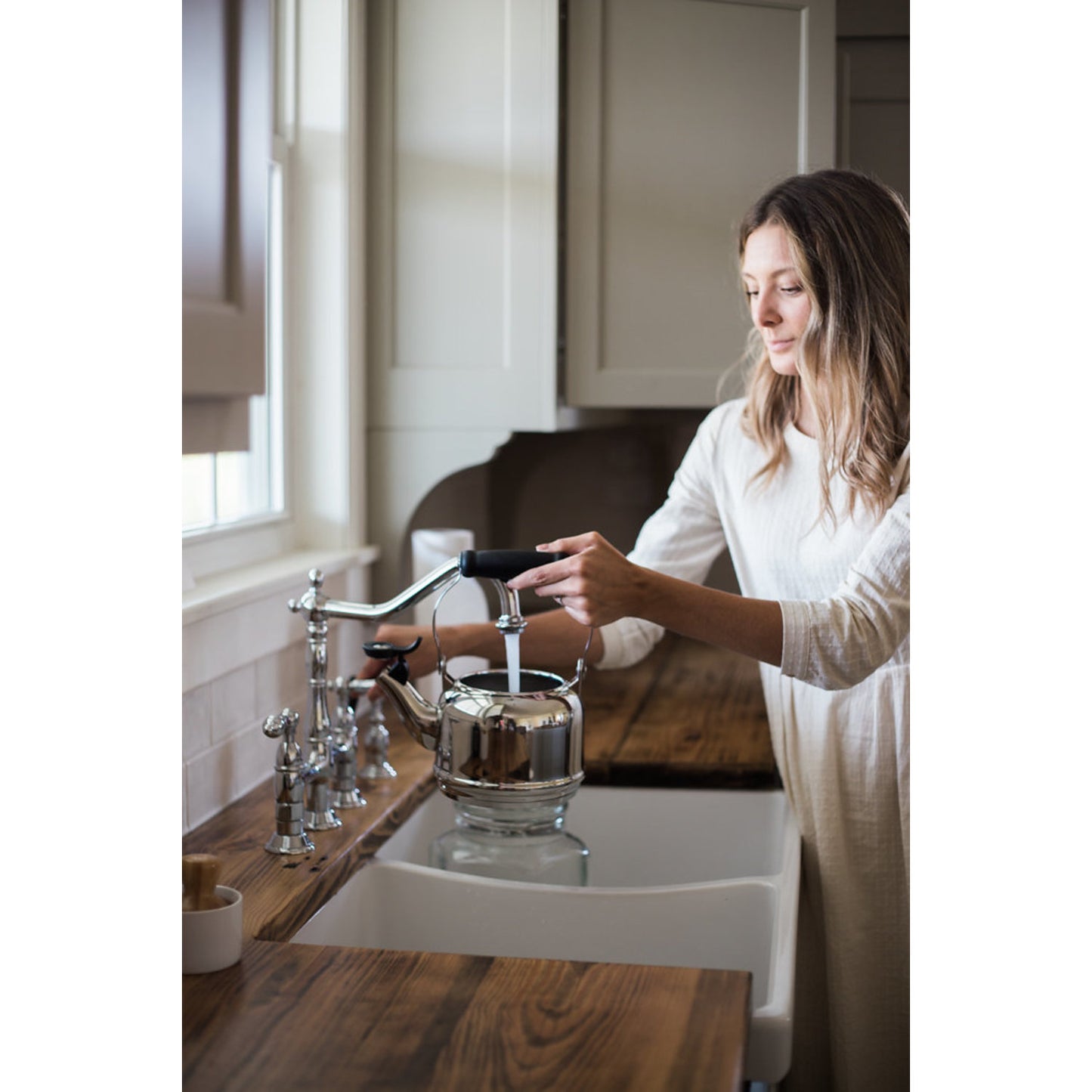 KINGSTON Brass Heritage Bridge Kitchen Faucet with Brass Sprayer in use by a woman next to a sink.