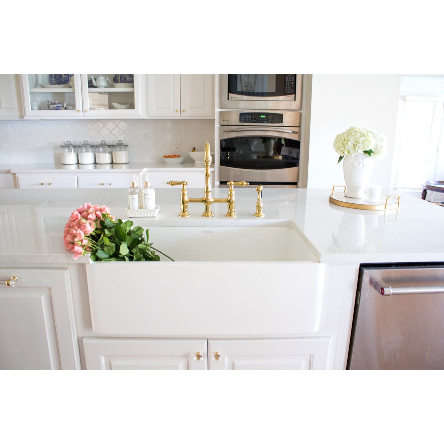 Modern kitchen with white countertops, Kingston Brass KS1272ALBS polished brass faucets, farmhouse sink, and decorative elements.