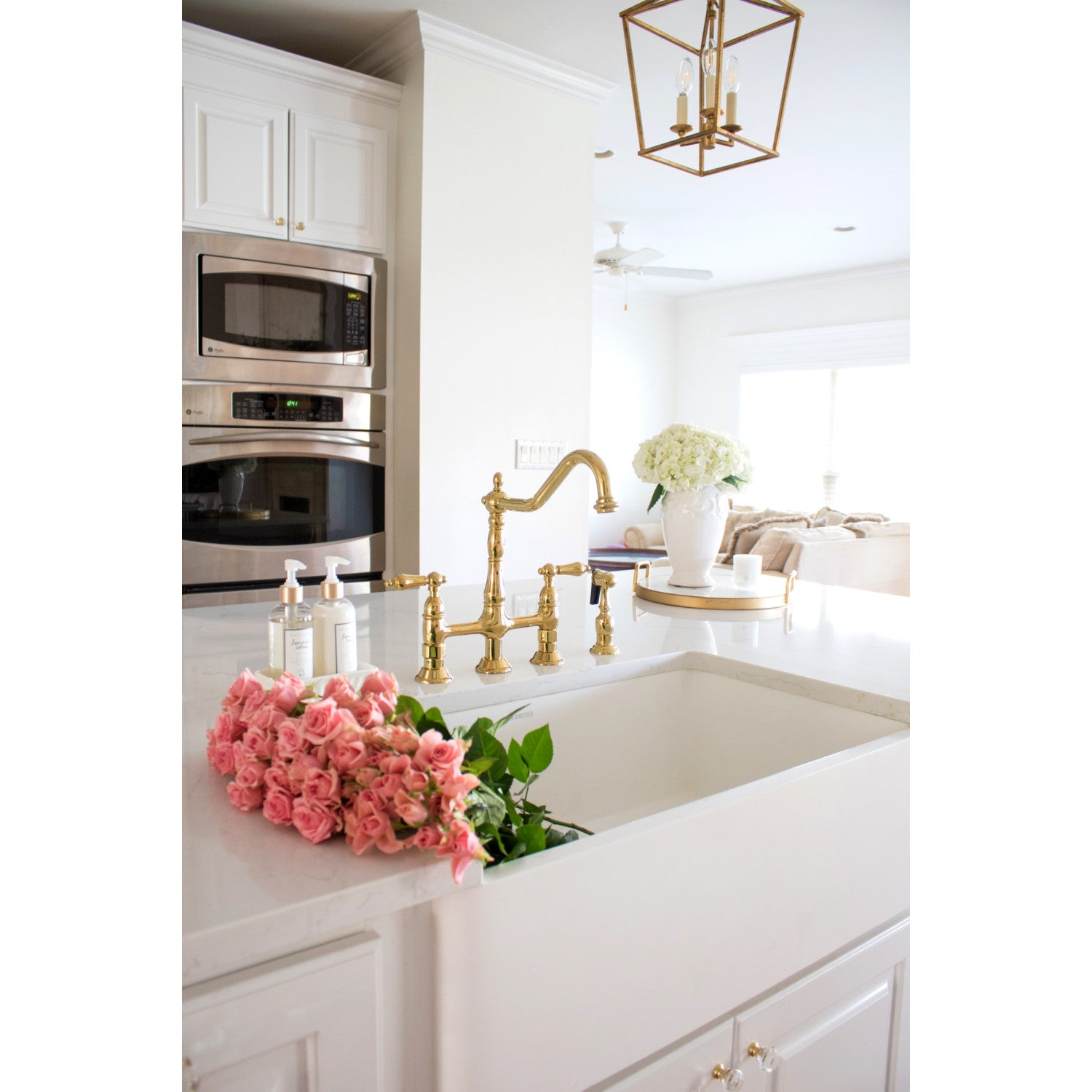 Modern kitchen with white countertops, Kingston Brass KS1272ALBS polished brass faucet, and pink flowers.