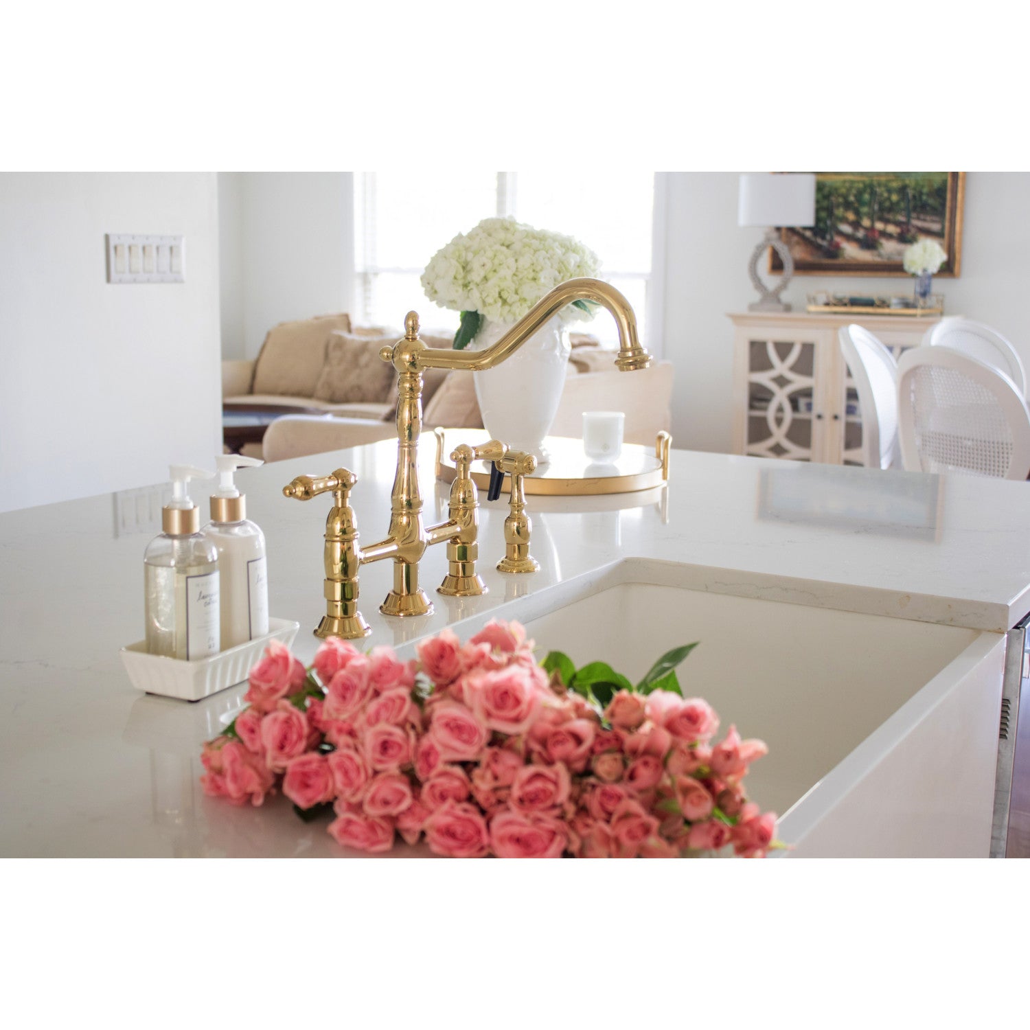Lifestyle image of Kingston Brass KS1272ALBS polished brass kitchen faucet in white kitchen with pink roses, and decorative bottles.