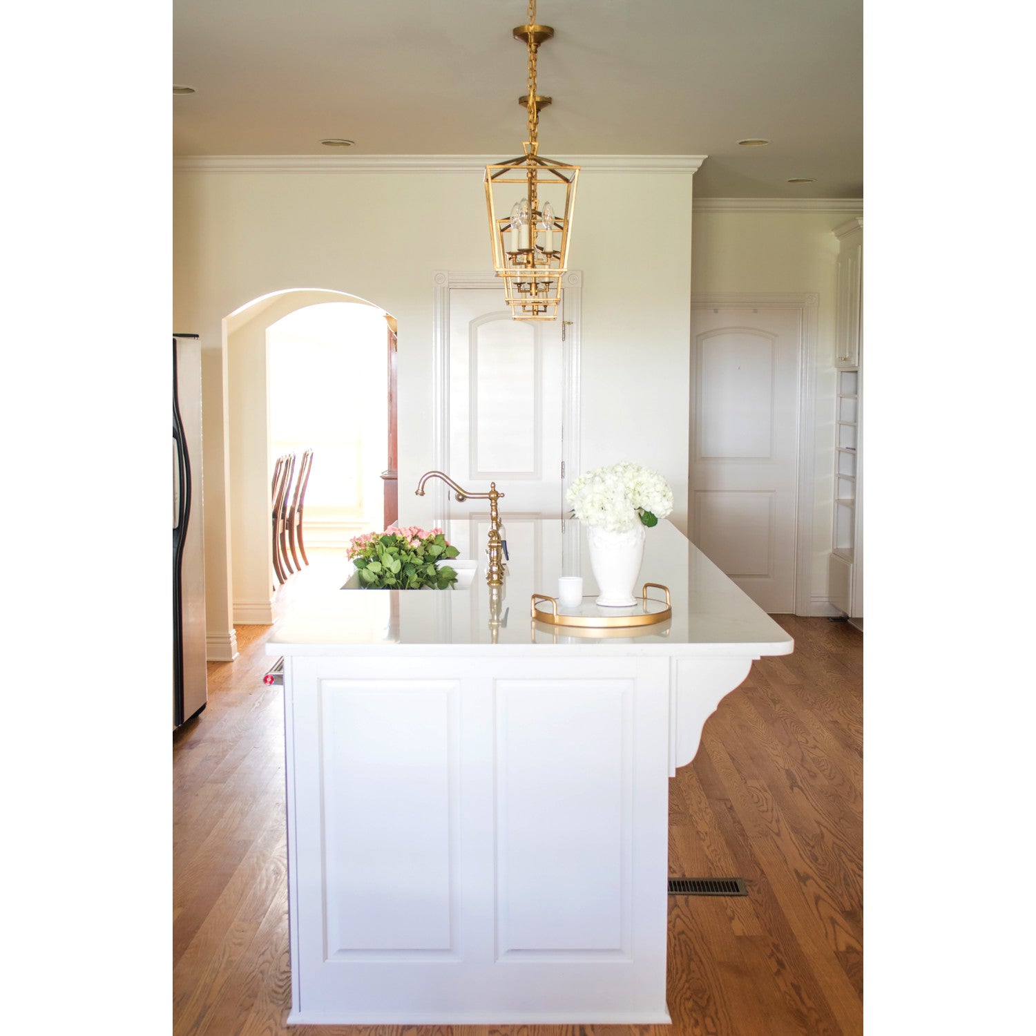 Kingston Brass KS1272ALBS polished brass kitchen faucet in a modern kitchen island, with brass pendant light, and wooden flooring.