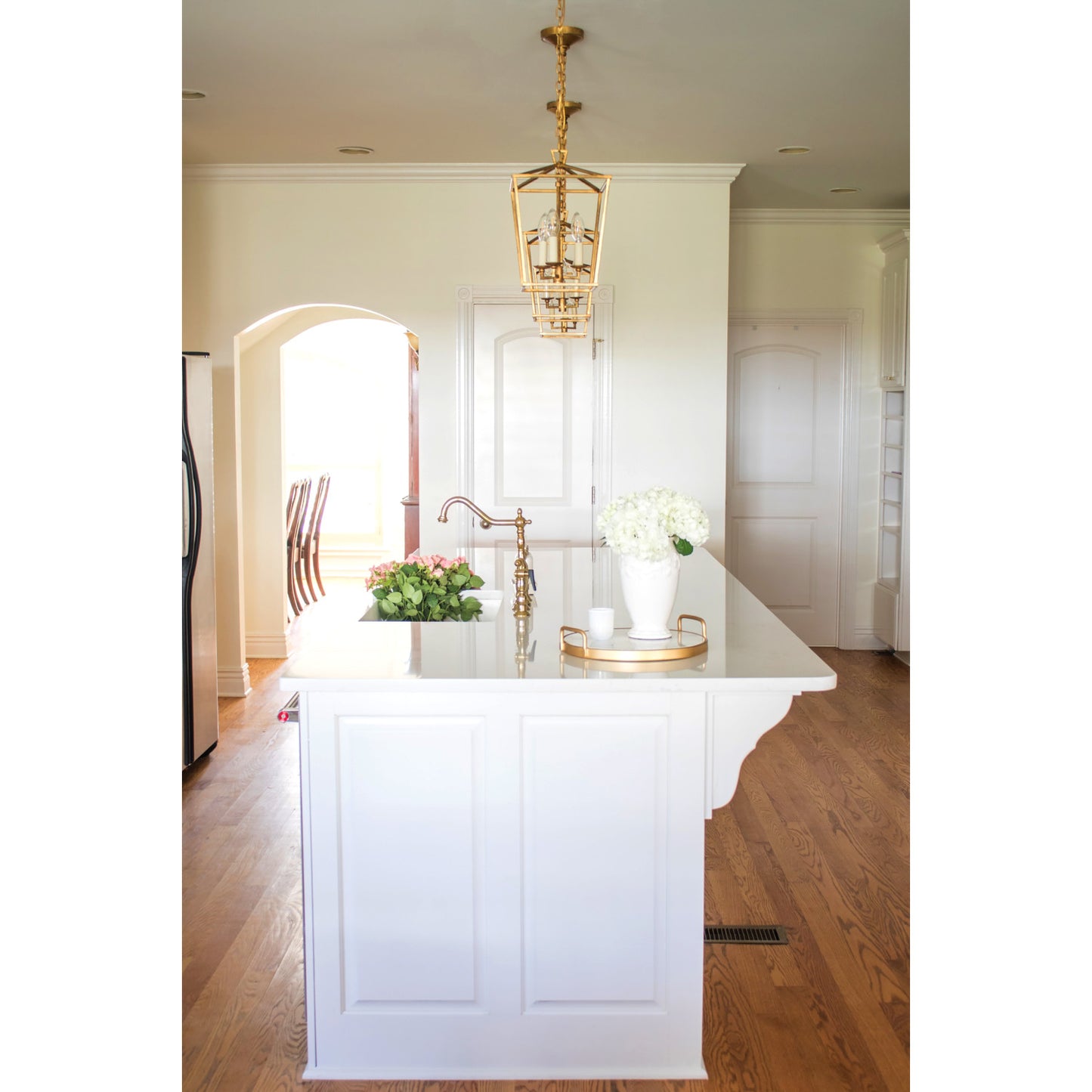 Kingston Brass KS1272ALBS polished brass kitchen faucet in a modern kitchen island, with brass pendant light, and wooden flooring.