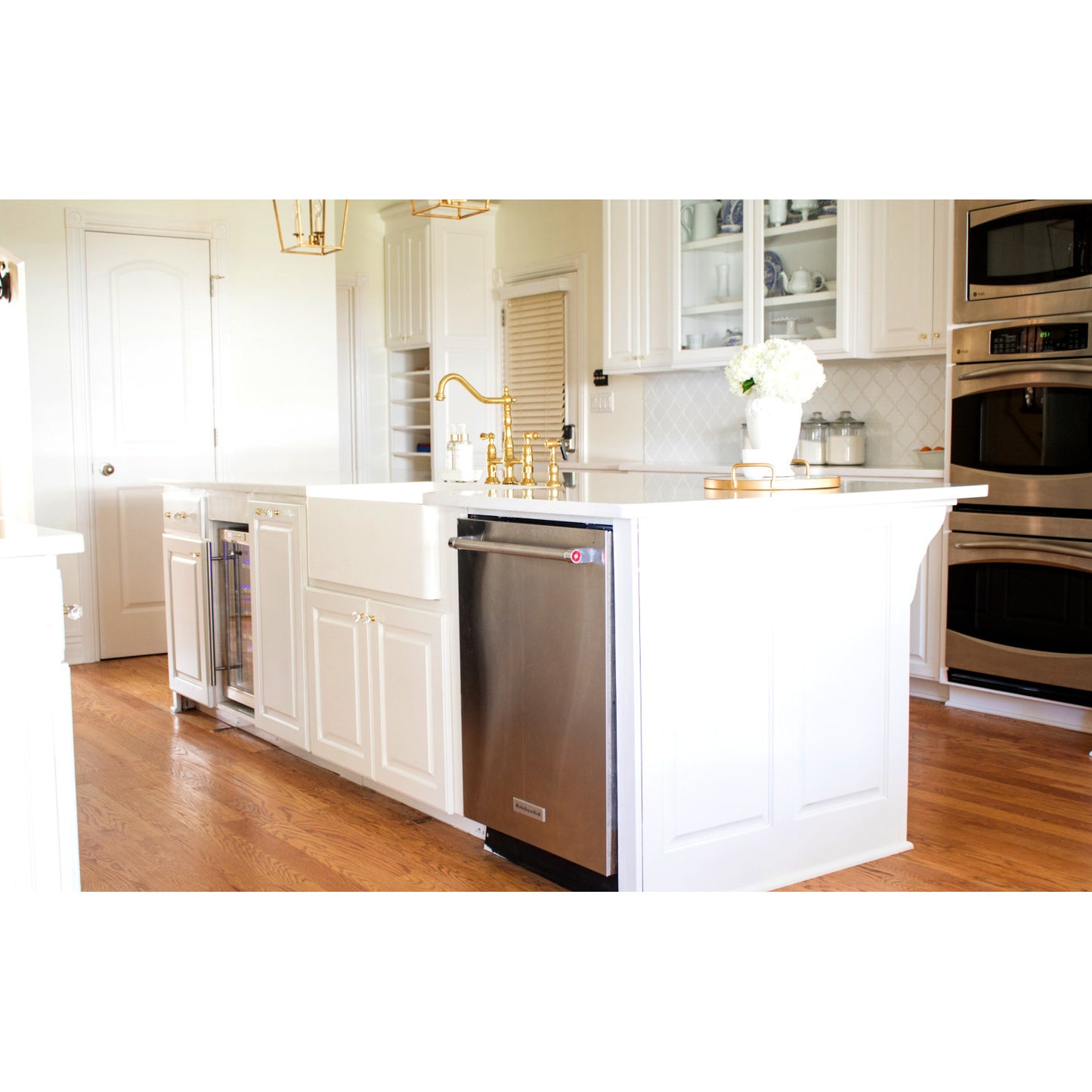 Modern kitchen island with Kingston Brass KS1272ALBS polished brass faucet, white cabinets, and wooden flooring.