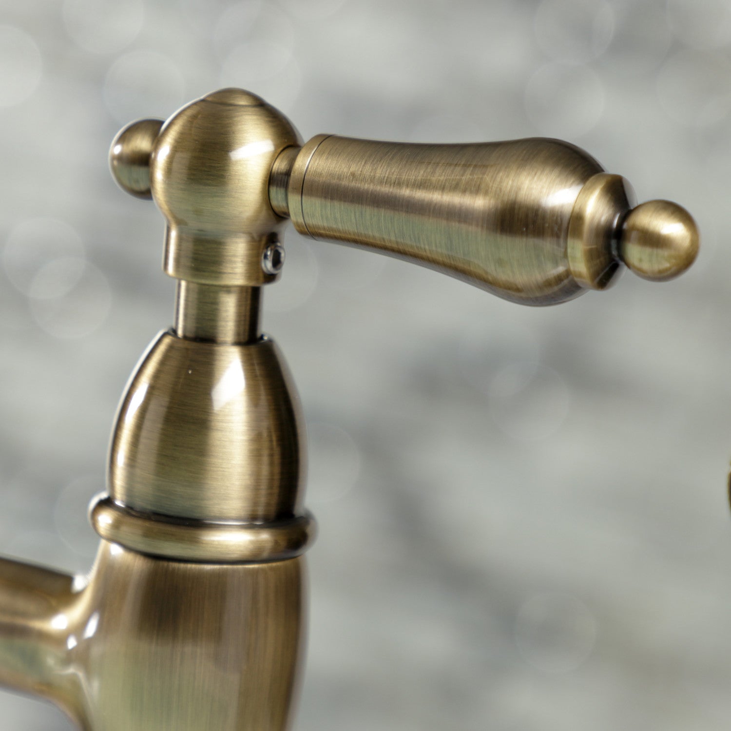 Close-up of Kingston Brass KS1273ALBS antique brass faucet handle against a blurred background
