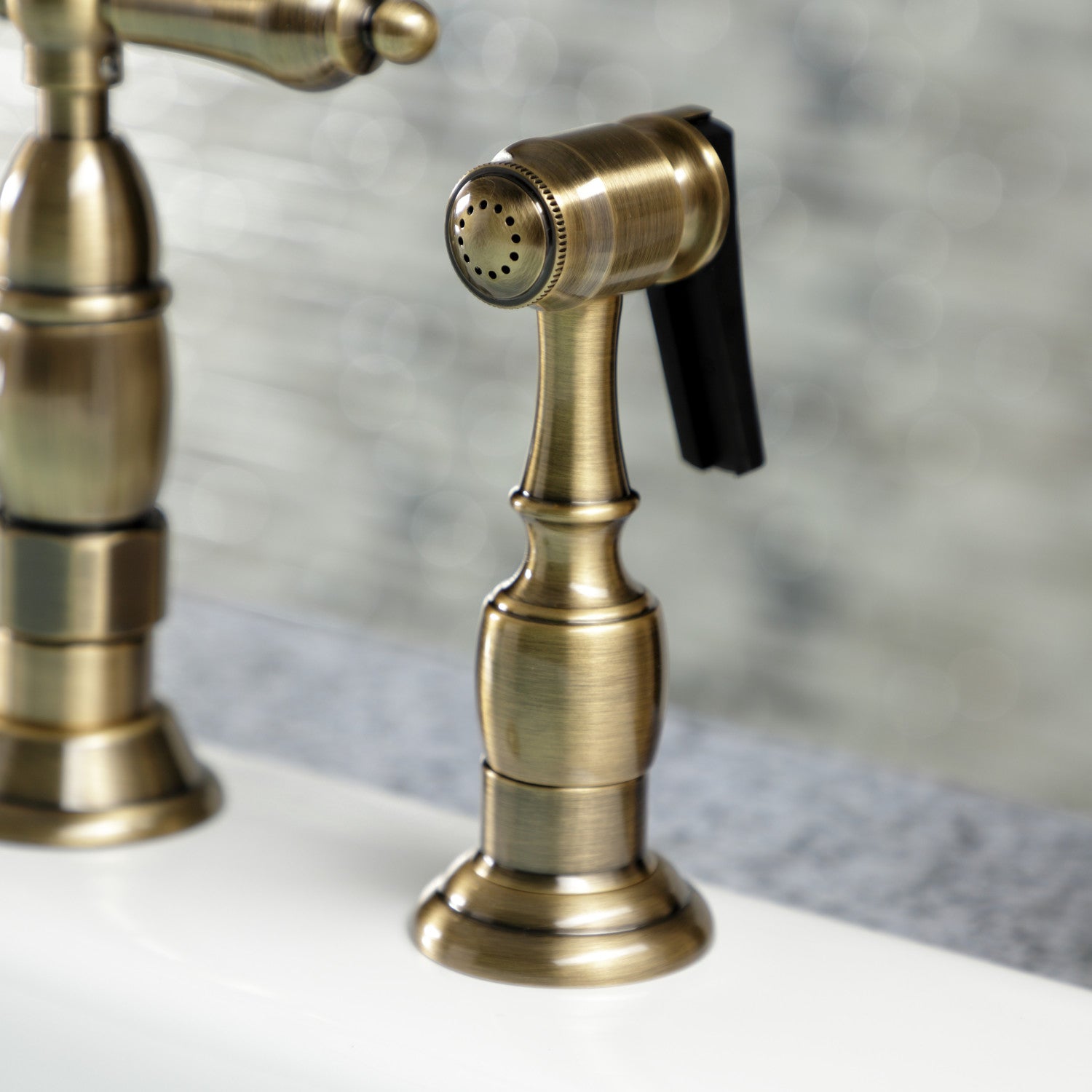 Kingston Brass KS1273ALBS antique brass kitchen faucet with close up of spray head on a white countertop
