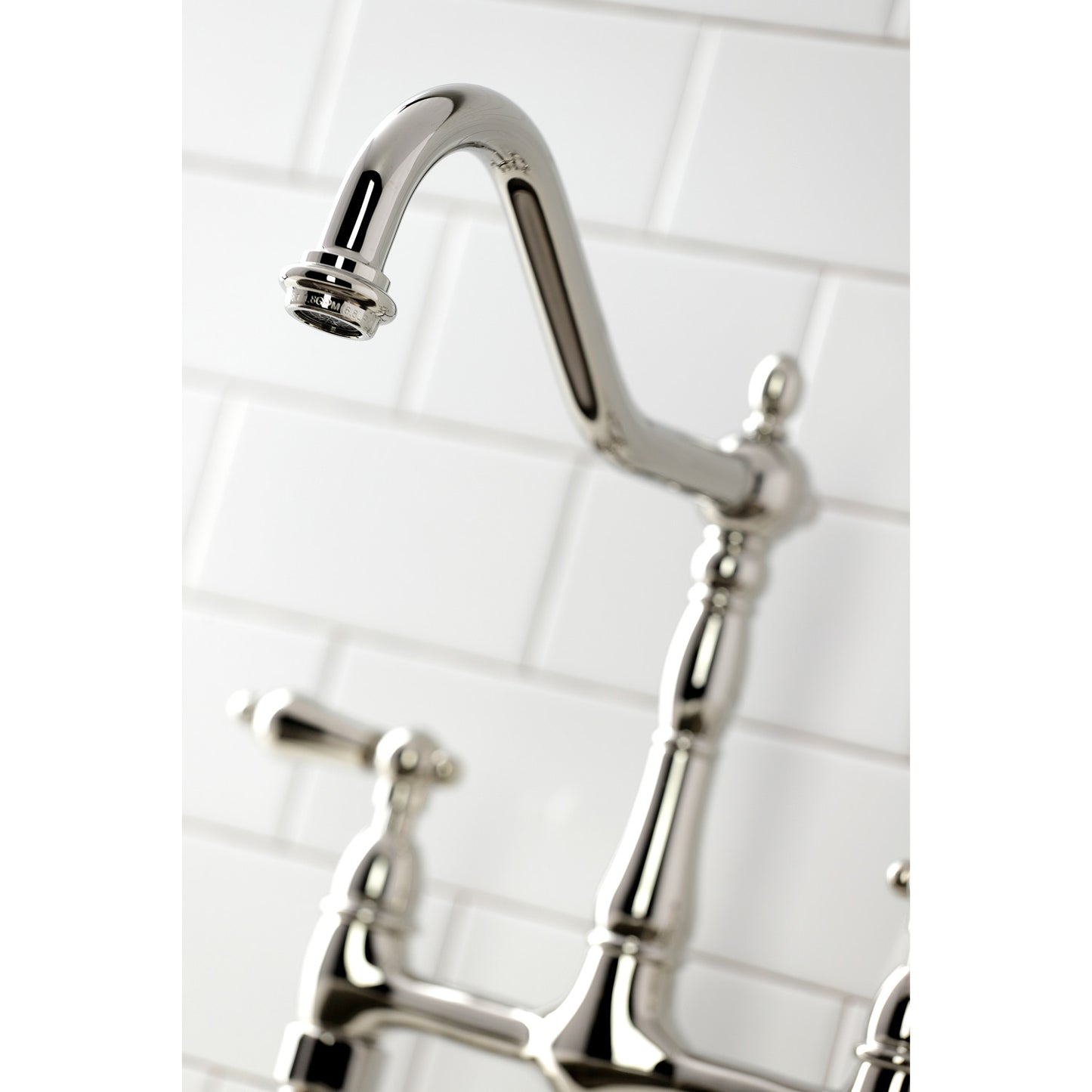 Close-up of the spout of KINGSTON Brass Heritage Bridge Kitchen Faucet with Brass Sprayer against white tiled background.
