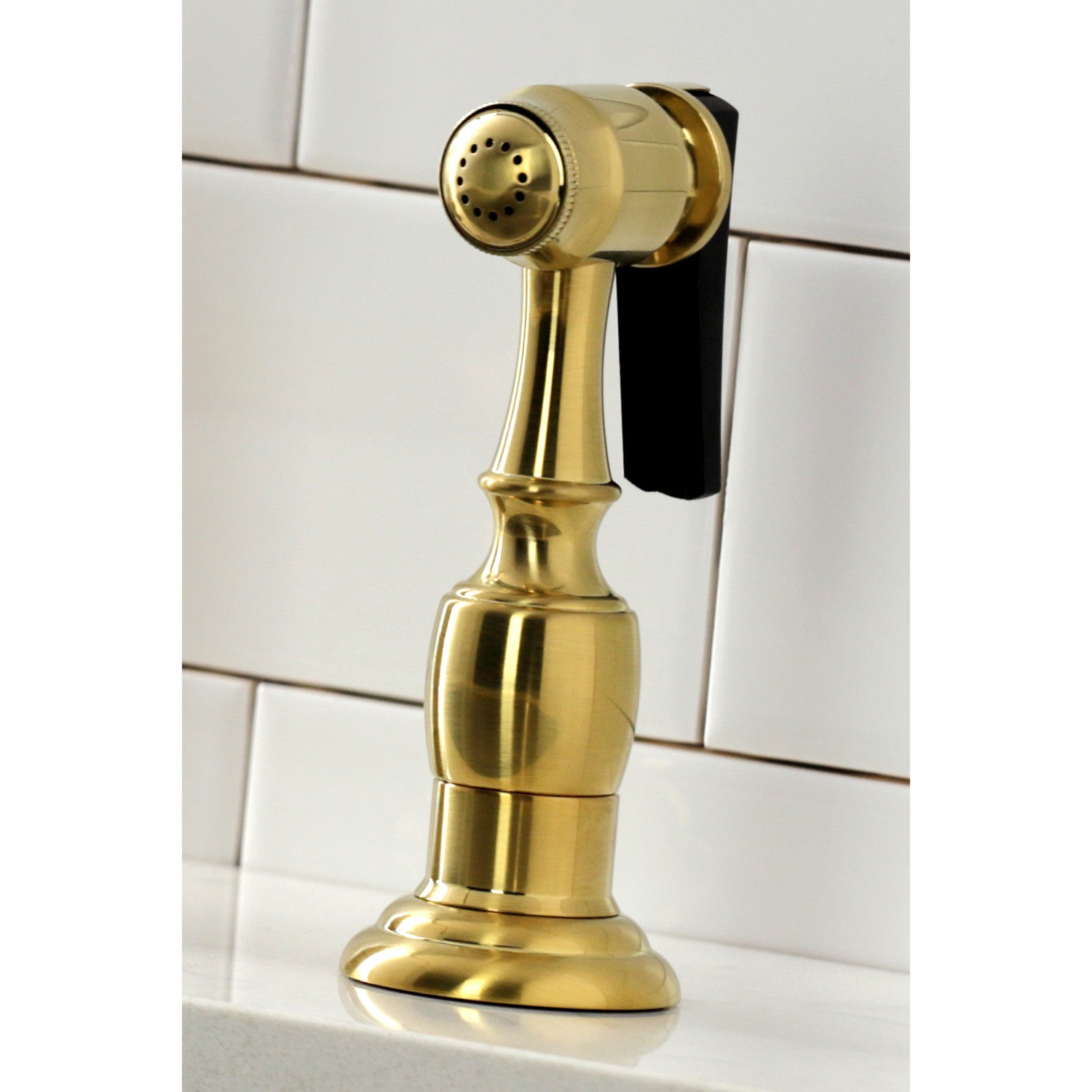 Close up of Kingston Brass KS1277ALBS brushed brass kitchen faucet sprayer on a white tiled background