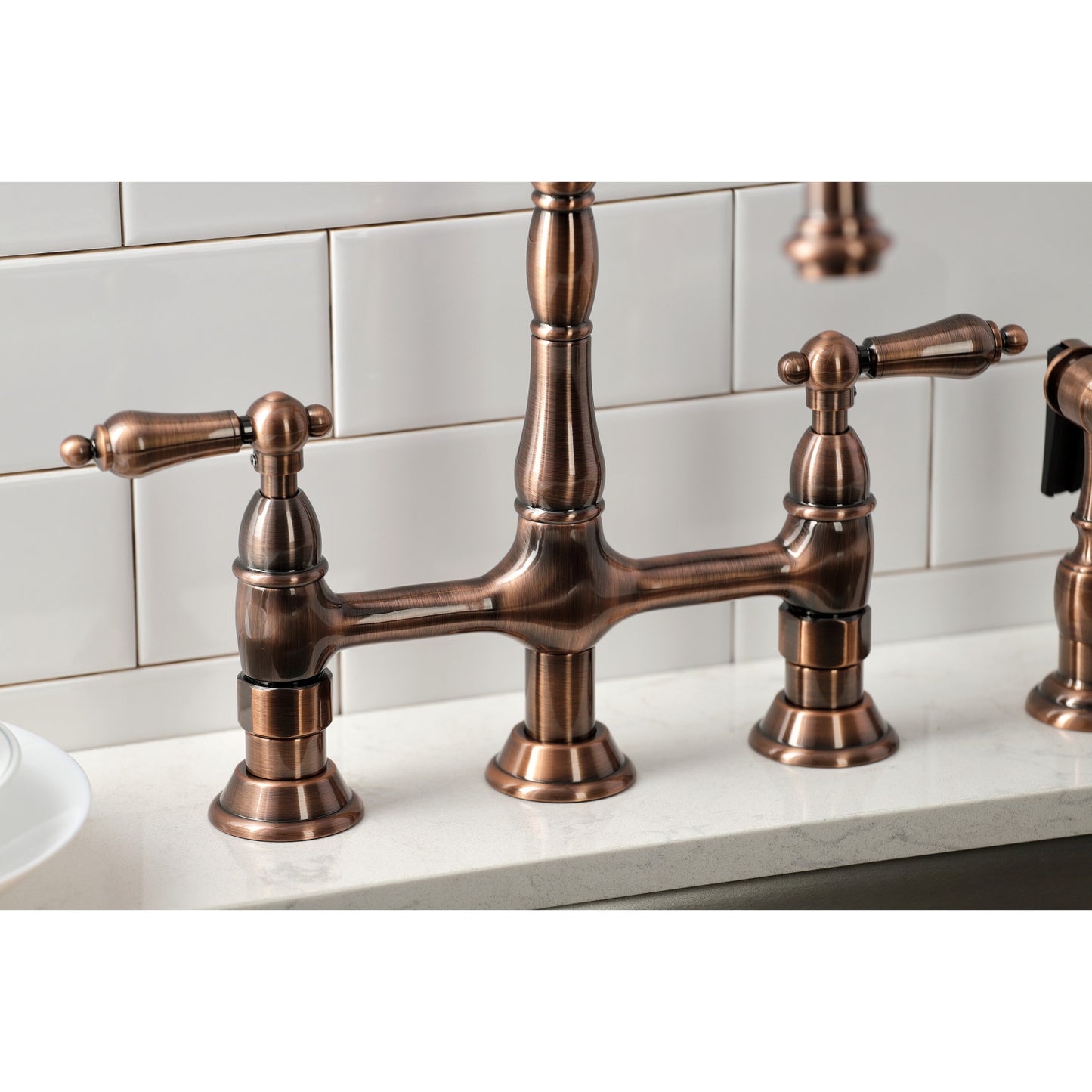 Kingston Brass KS127ALBSAC antique copper bridge faucet set on a white countertop with a tiled wall background