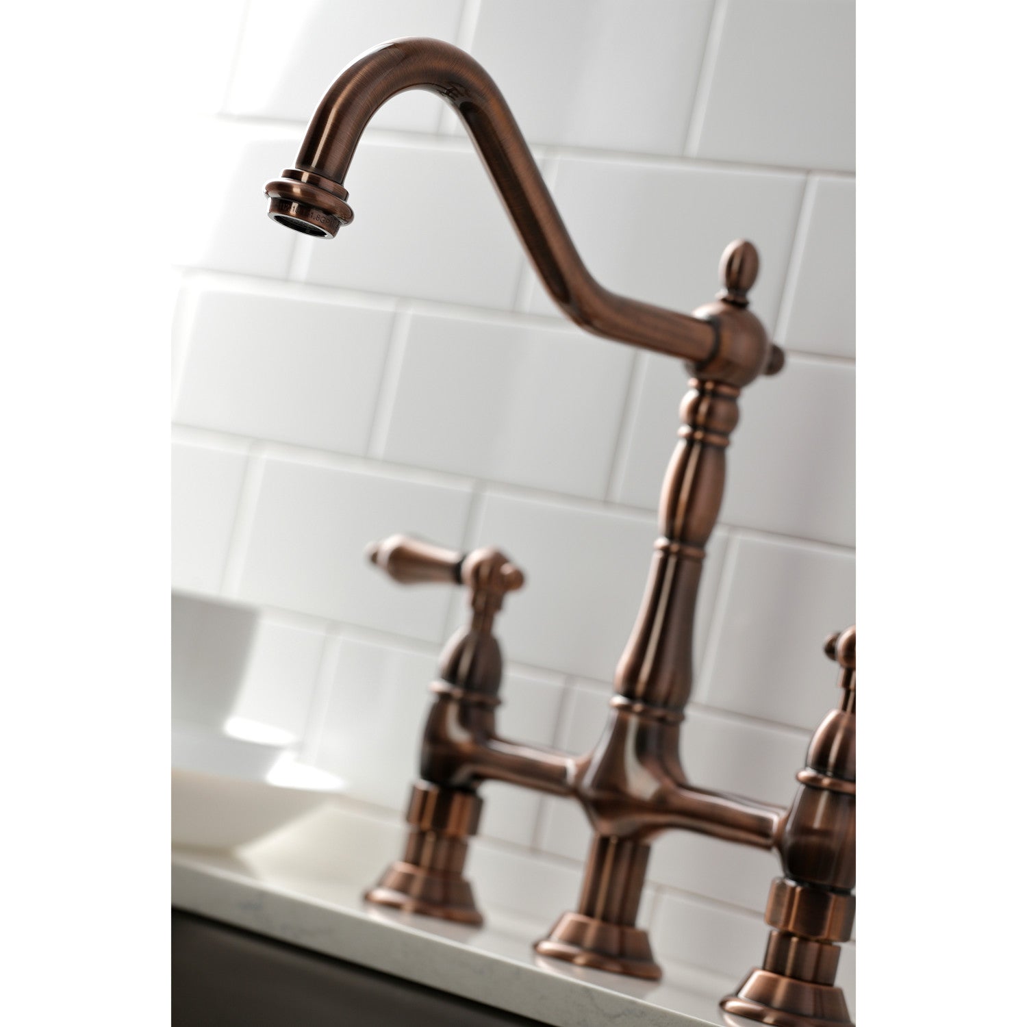 Close up of faucet head for Kingston Brass KS127ALBSAC antique copper kitchen faucet on a white tiled wall