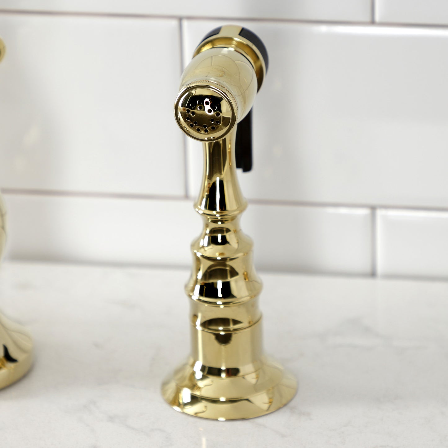 Kingston Brass KS7752AXBS polished brass side spray faucet against a white tiled wall