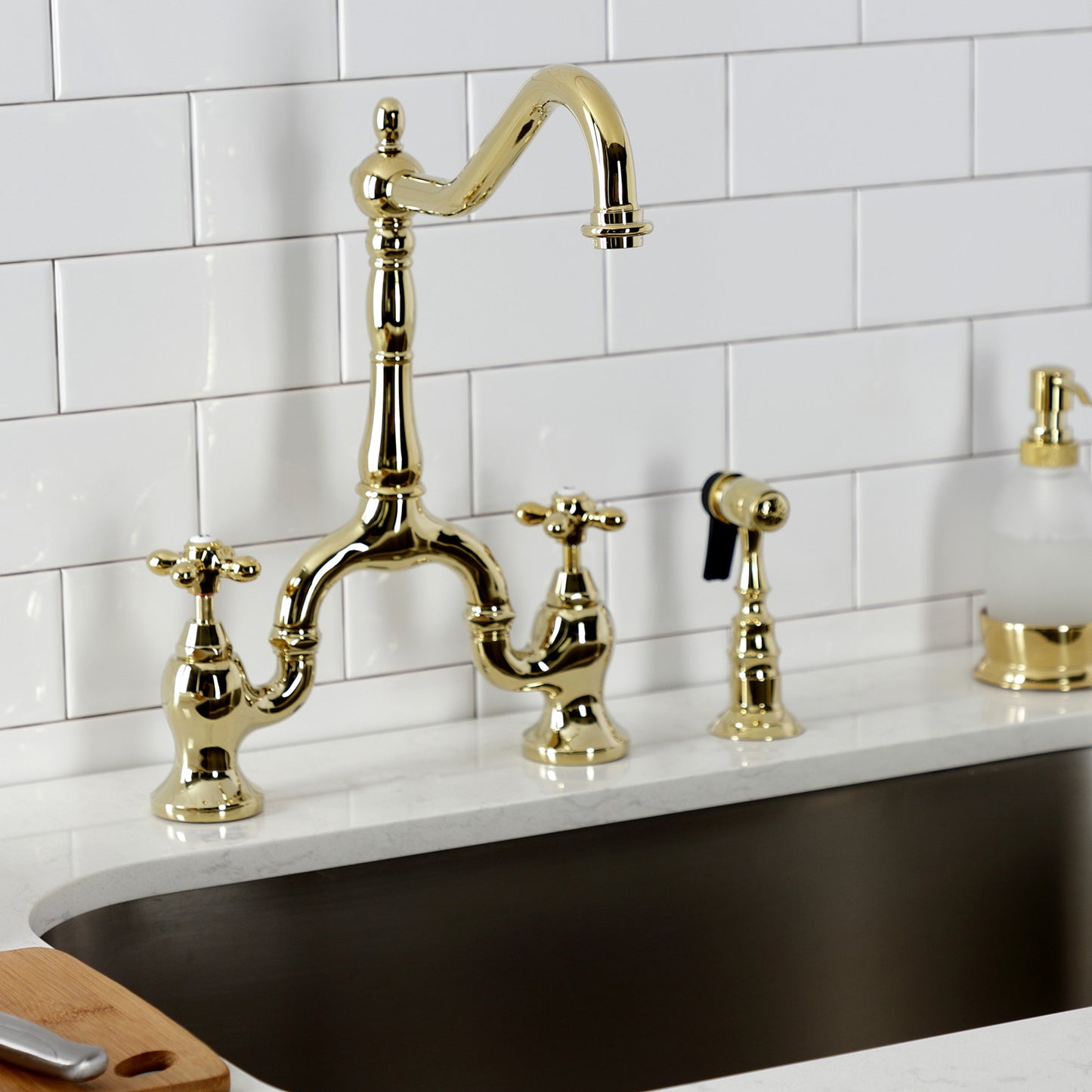 Kingston Brass KS7752AXBS polished brass faucet set on a kitchen sink with white tiled wall background