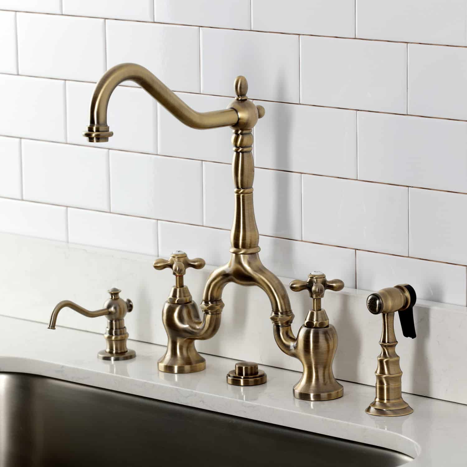 Kingston Brass KS7753AXBS Antique Brass kitchen faucet set against a white tiled wall