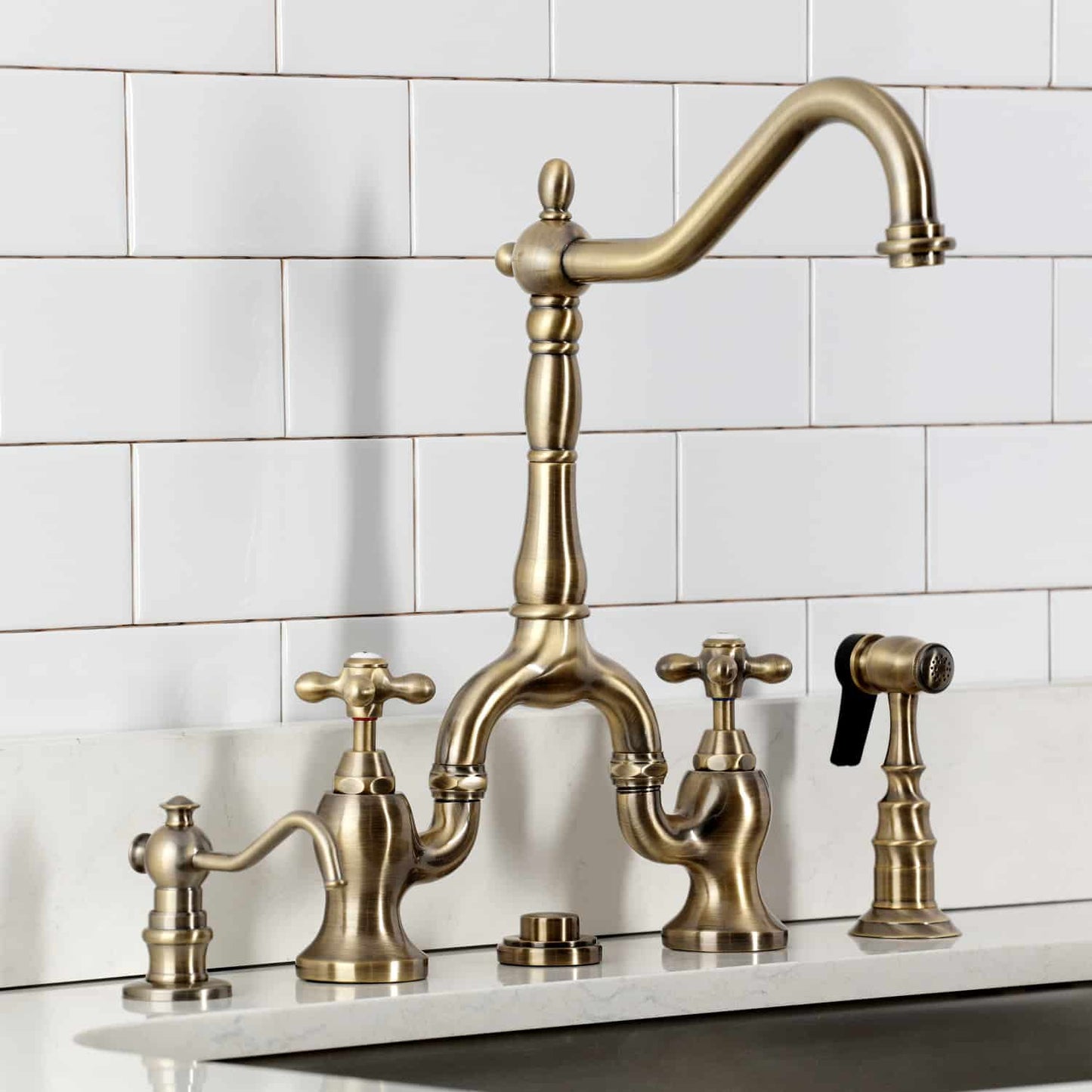 Kingston Brass KS7753AXBS Antique Brass kitchen faucet set against a white tiled wall