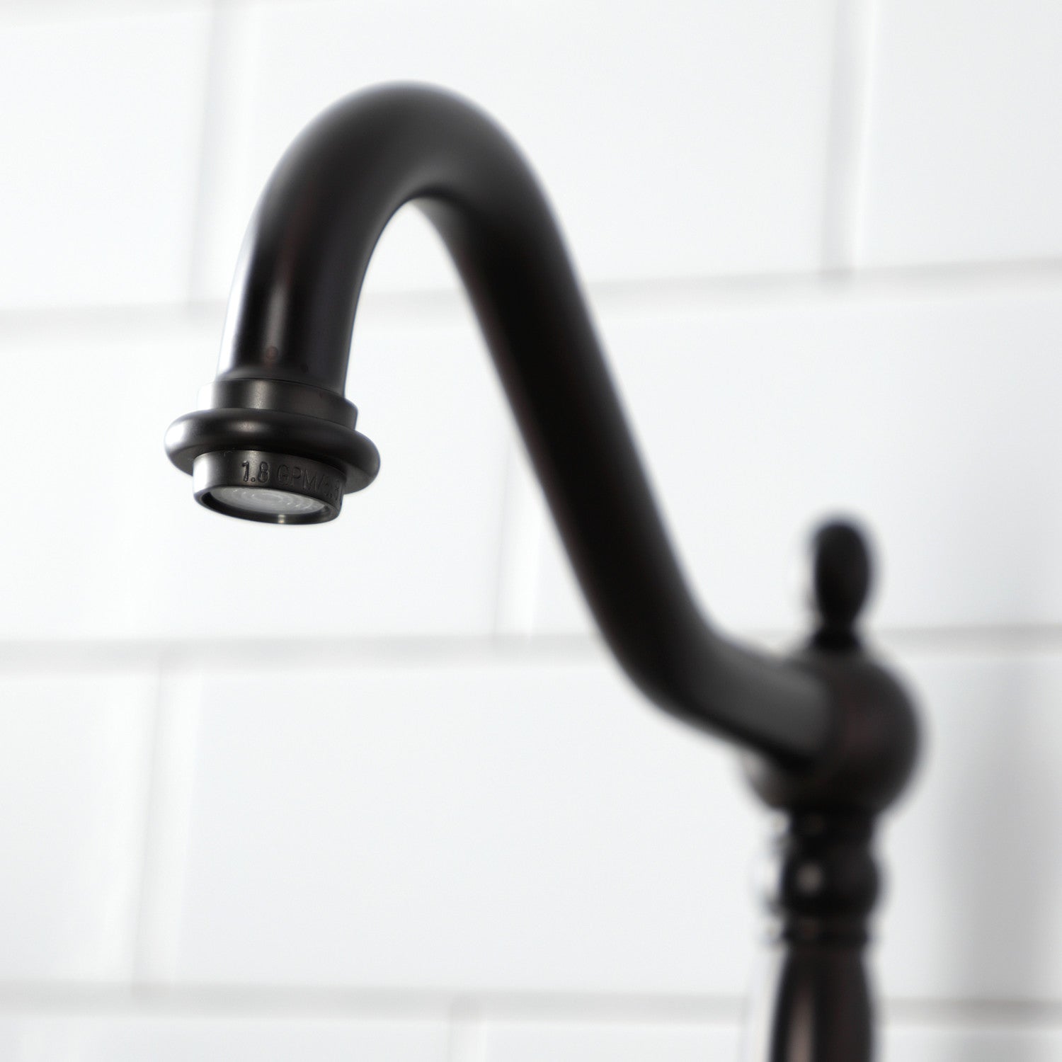 Detail of Kingston Brass KS7755AXBS oil rubbed bronze kitchen bridge faucet against a white tiled wall