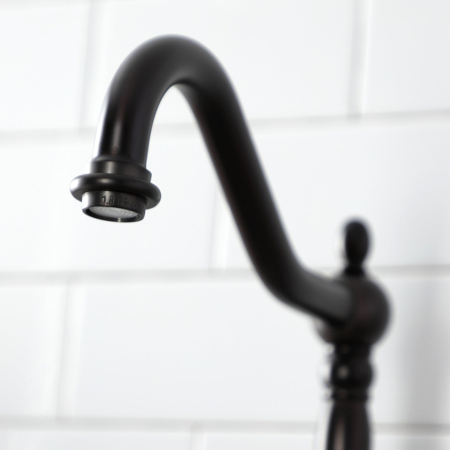 Close-up of the Kingston Brass English Country Deck Mount Bridge Kitchen Faucet spout against a white tiled background.