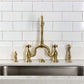 Kingston Brass KS7757AXBS Brushed Brass Kitchen faucet set on a kitchen sink with white tiled wall background