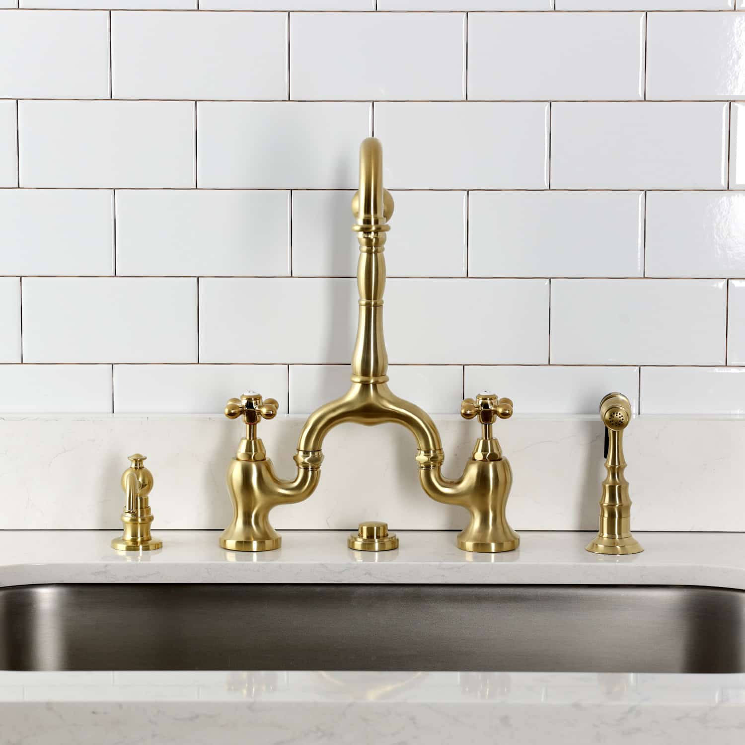 Kingston Brass KS7757AXBS Brushed Brass Kitchen faucet set on a kitchen sink with white tiled wall background