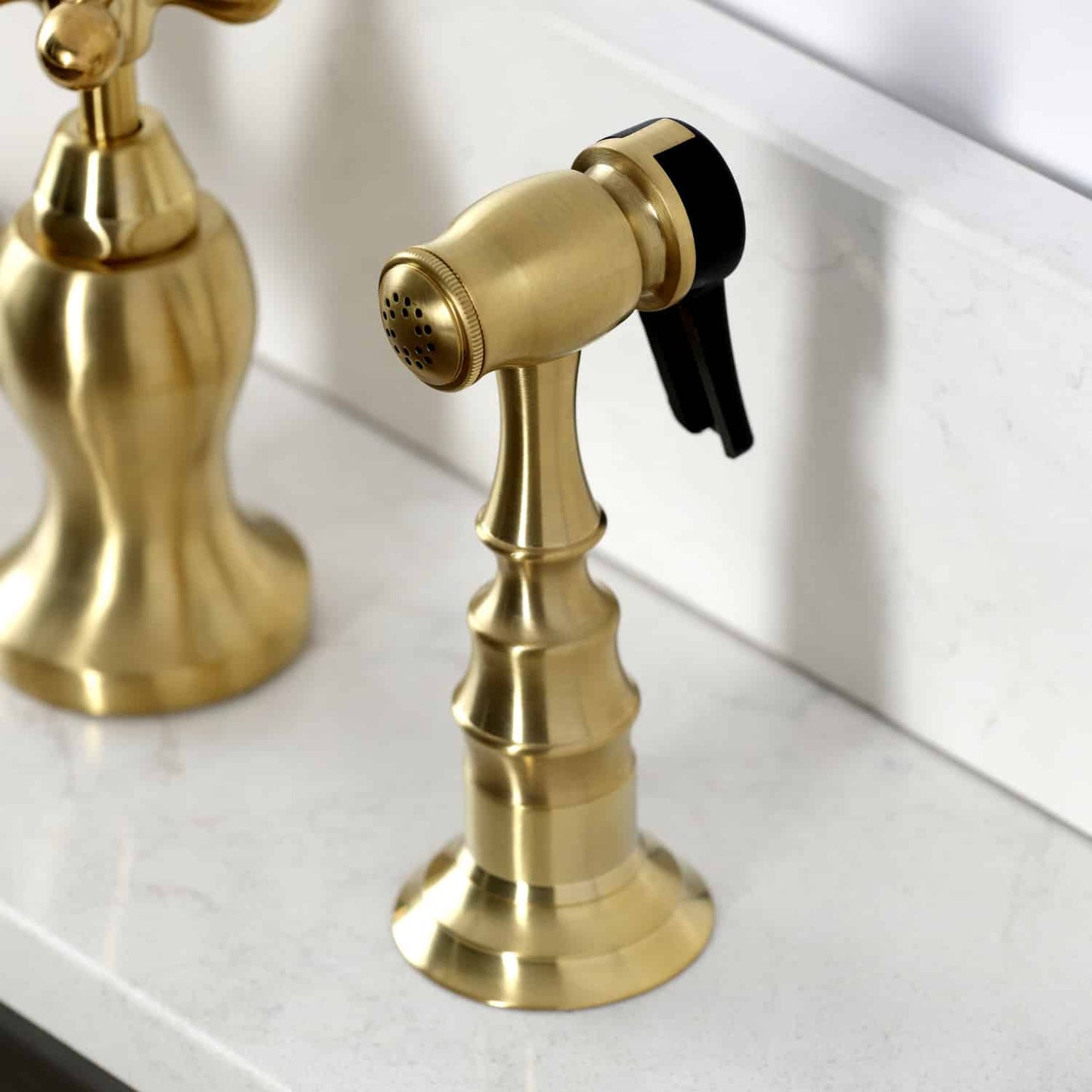 Kingston Brass KS7757AXBS Brushed Brass kitchen faucet showing side spray head on a white countertop