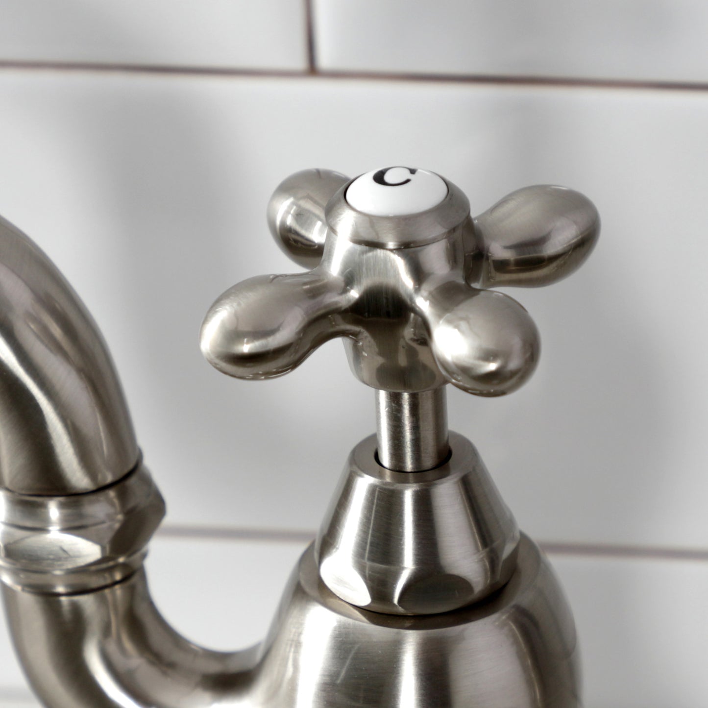 Close-up of the handle of Kingston Brass English Country Deck Mount Bridge Kitchen Faucet featuring a unique cross design.