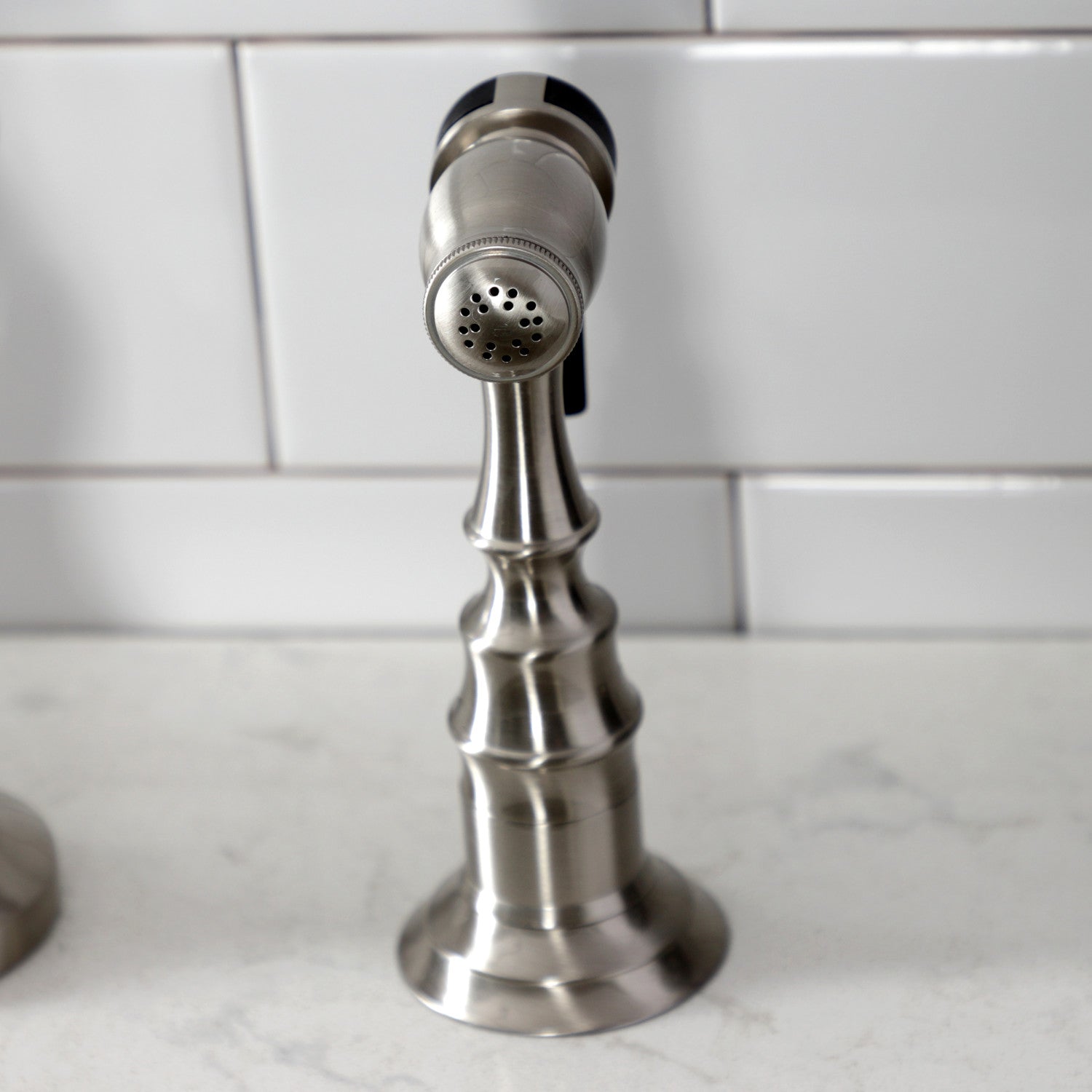 Kingston Brass KS7758AXBS brushed nickel kitchen side spray faucet on a marble countertop with tiled wall background