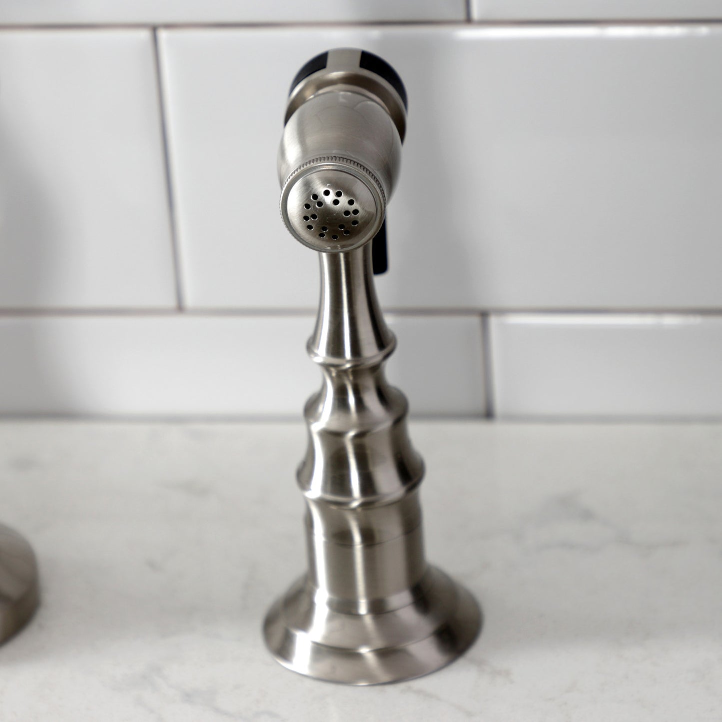 Kingston Brass English Country Deck Mount Bridge Kitchen Faucet close-up view of the spout top on marble countertop