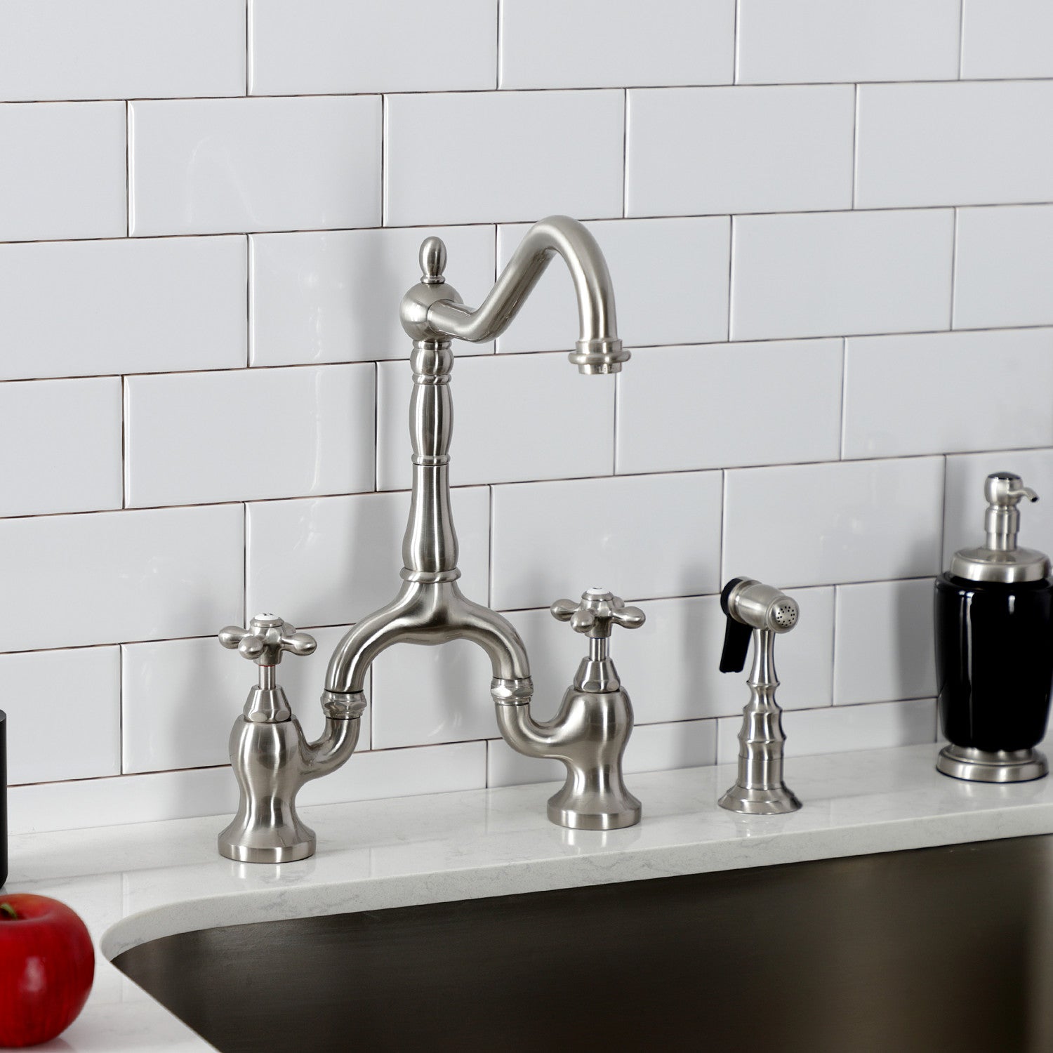 Kingston Brass KS7758AXBS brushed nickel kitchen faucet set in a quartz countertop against a white tiled wall.