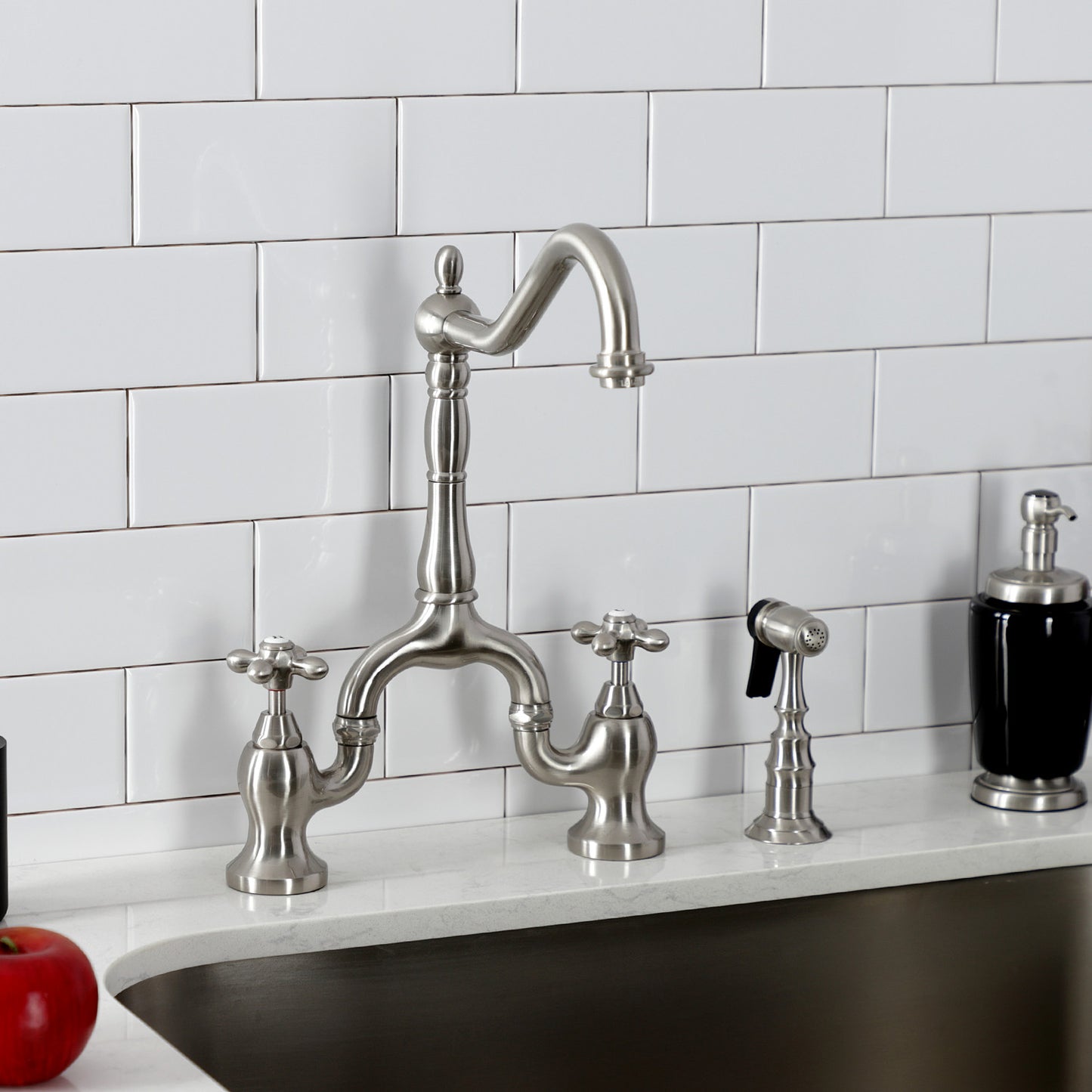 Kingston Brass KS7758AXBS brushed nickel kitchen faucet set in a quartz countertop against a white tiled wall.