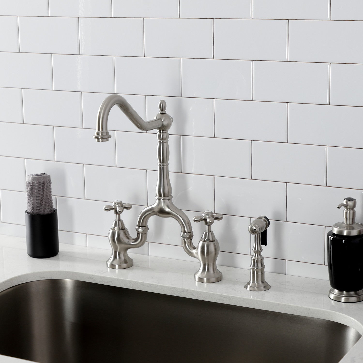 Kingston Brass KS7758AXBS brushed nickel kitchen faucet with handles against a white tiled wall background