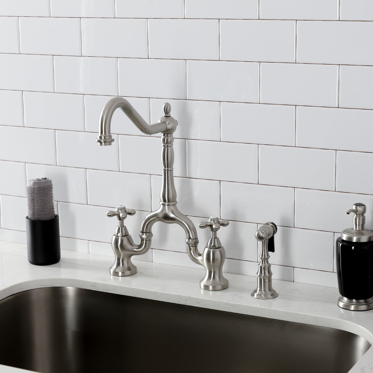 Kingston Brass KS7758AXBS brushed nickel kitchen faucet with handles against a white tiled wall background
